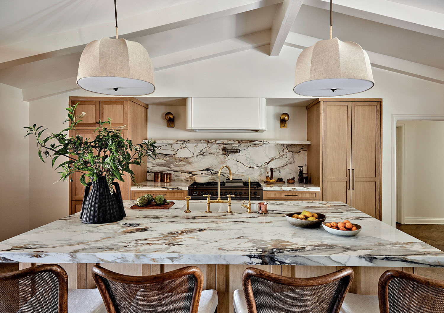 A kitchen island with bowls of fruit sitting on the marble counter and chairs sitting along the edge