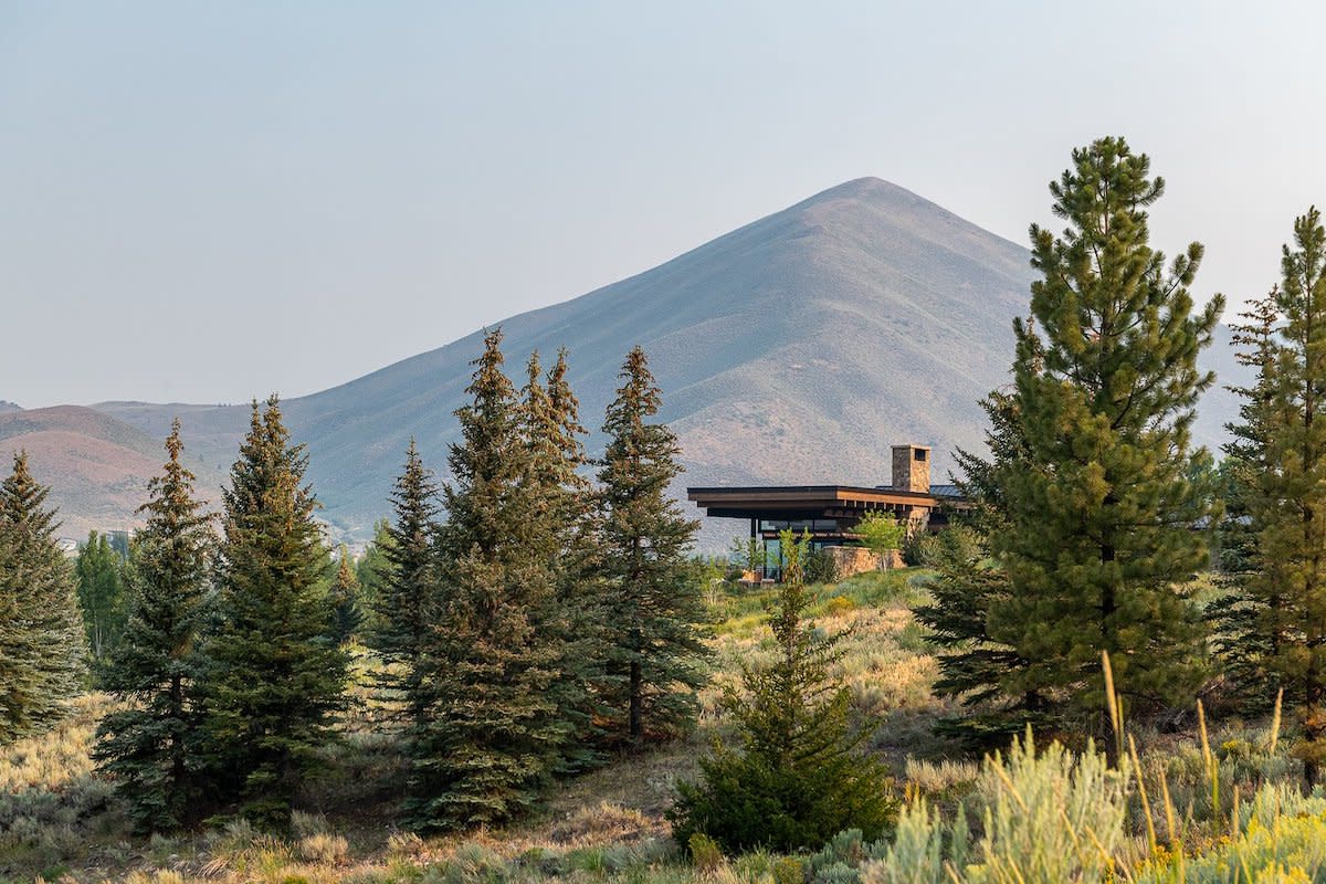 A picturesque mountain house nestled amidst lush green trees and grass.