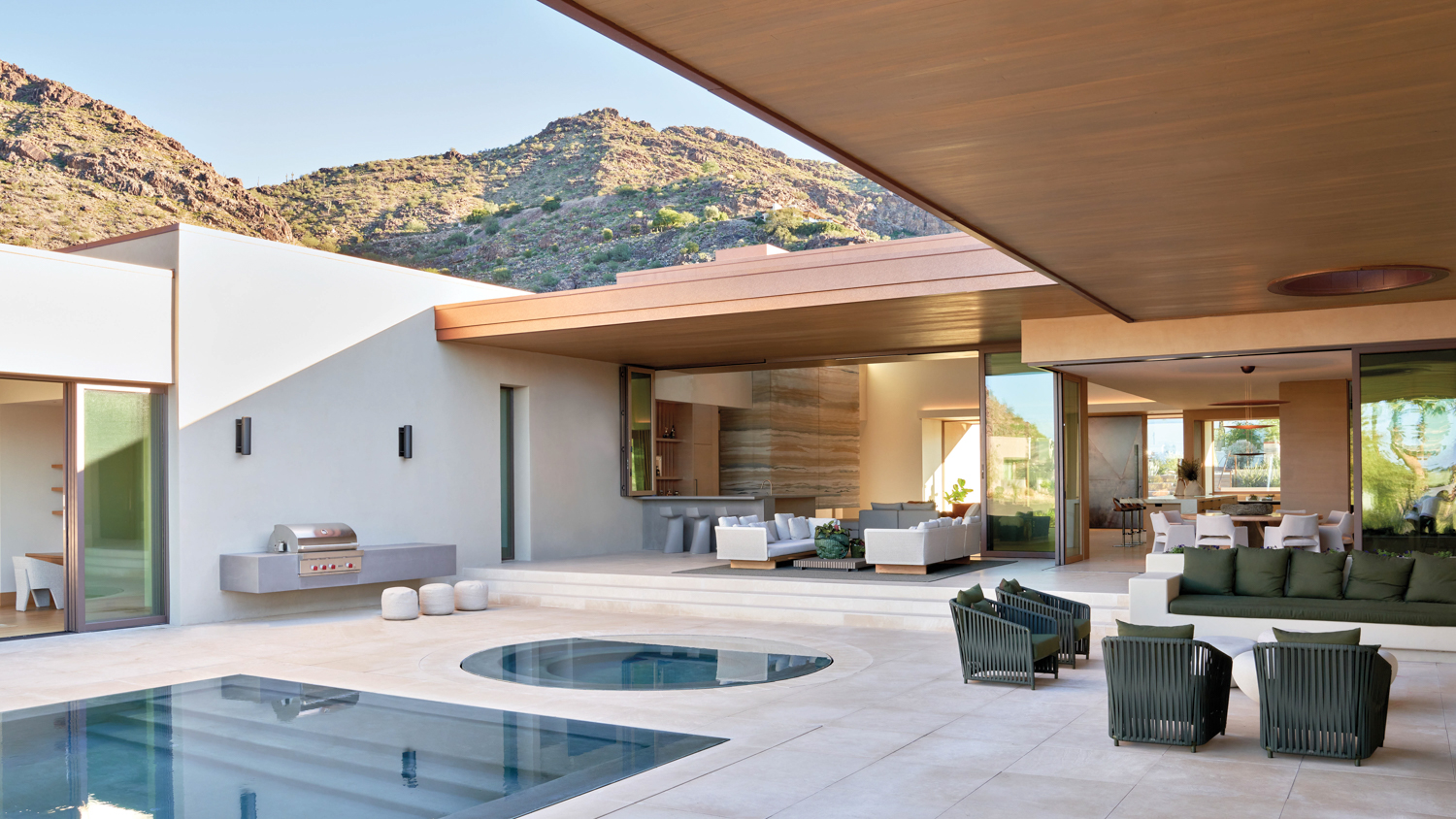 Indoor-outdoor living space that opens to a patio with a pool and jacuzzi in home by IMI Design