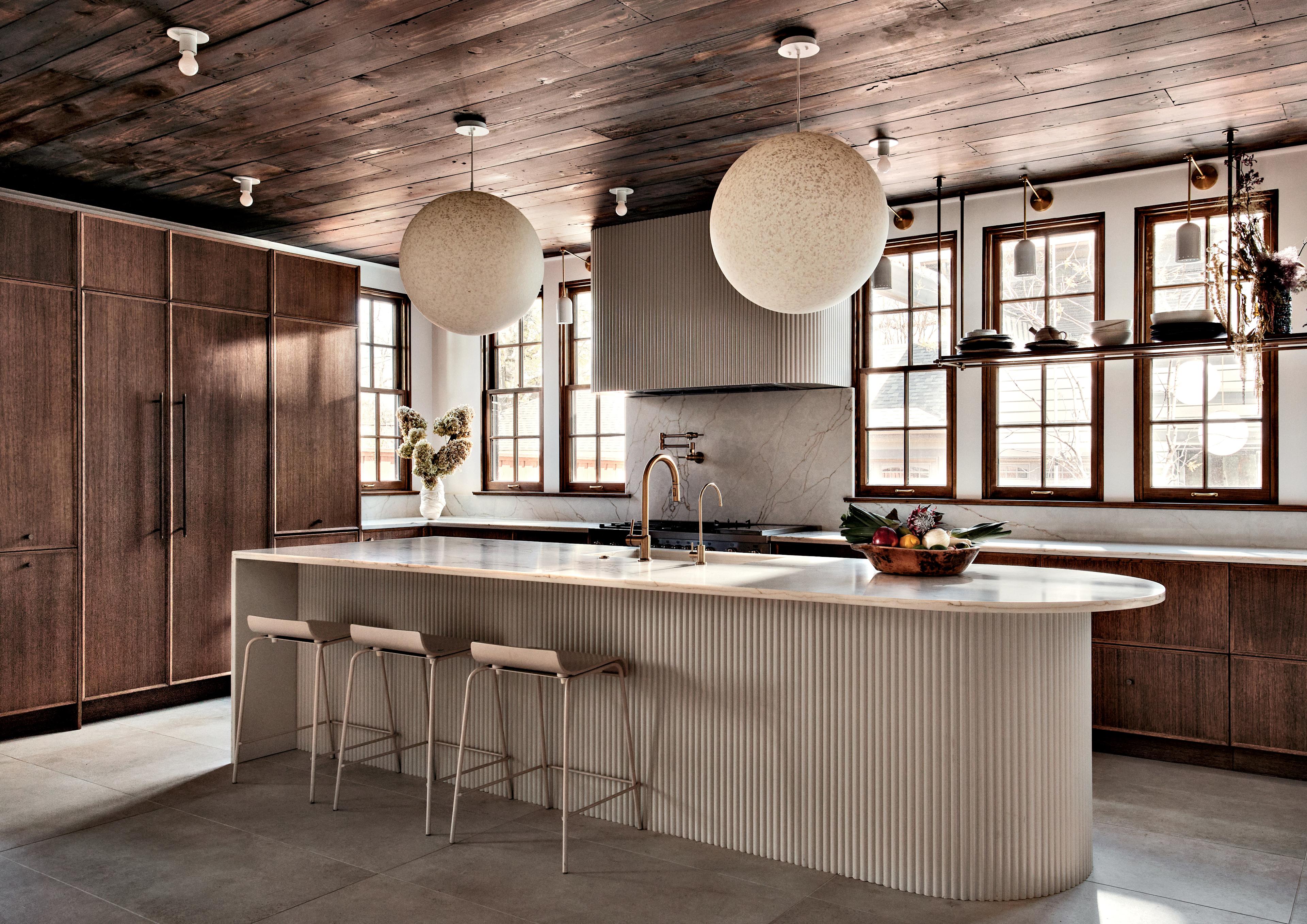 Walnut cabinetry, limestone flooring and quartz countertops in a kitchen with an island and stools.