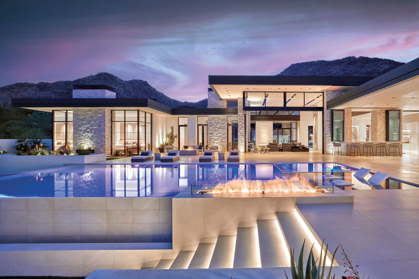 luxury home lit up at night with an outdoor pool in front of it