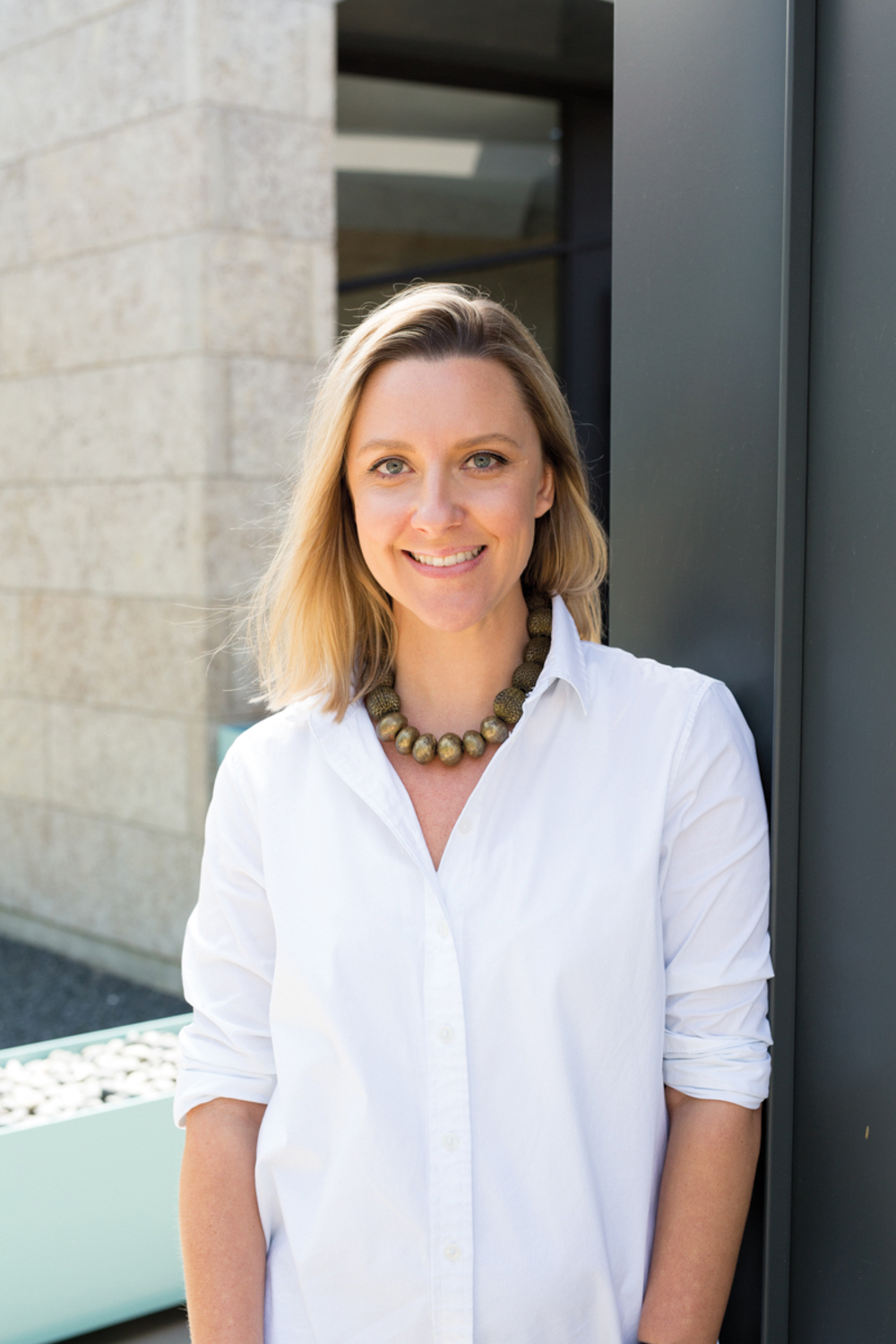 Kate Blocker standing in a white button-down shirt with a necklace.