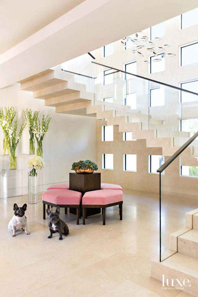 Louie (right) and Hermes greet guests in the entry. Interior designer Michael Fullen suspended an Ochre chandelier above a cantilevered staircase and arranged a custom modular bench upholstered in pink velvet by Pierre Frey from Kneedler Fauchere. The limestone flooring is by Solistone.