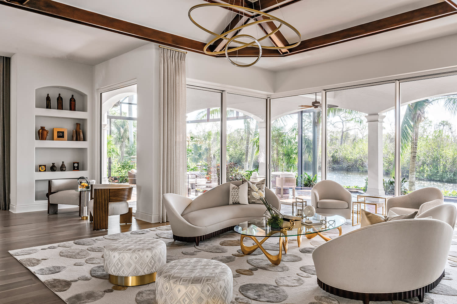 Luxurious living room with curved white sofas, oval coffee table, and large windows overlooking a lush garden.