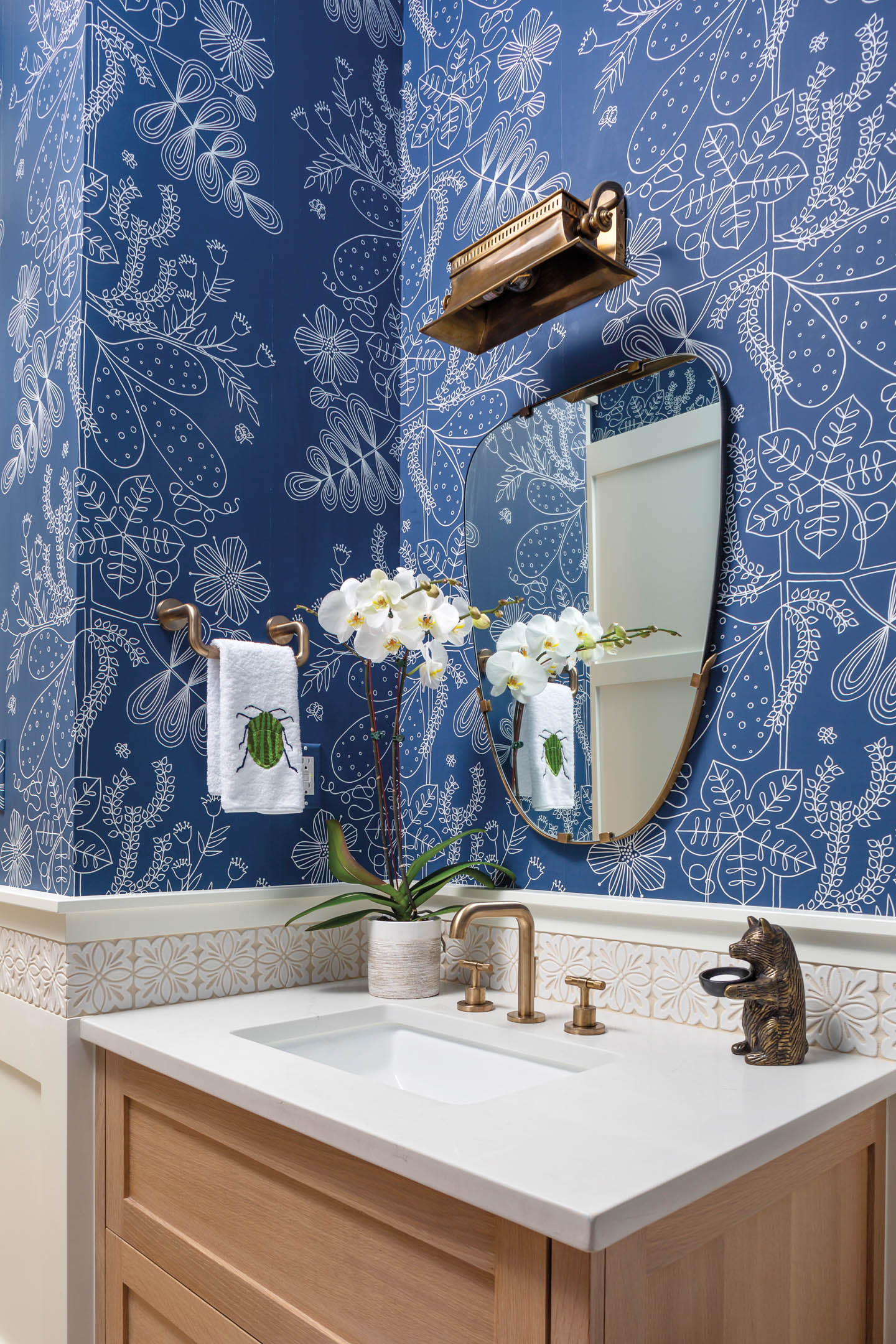 The powder room has a bright blue wallcovering and a brass light fixture.