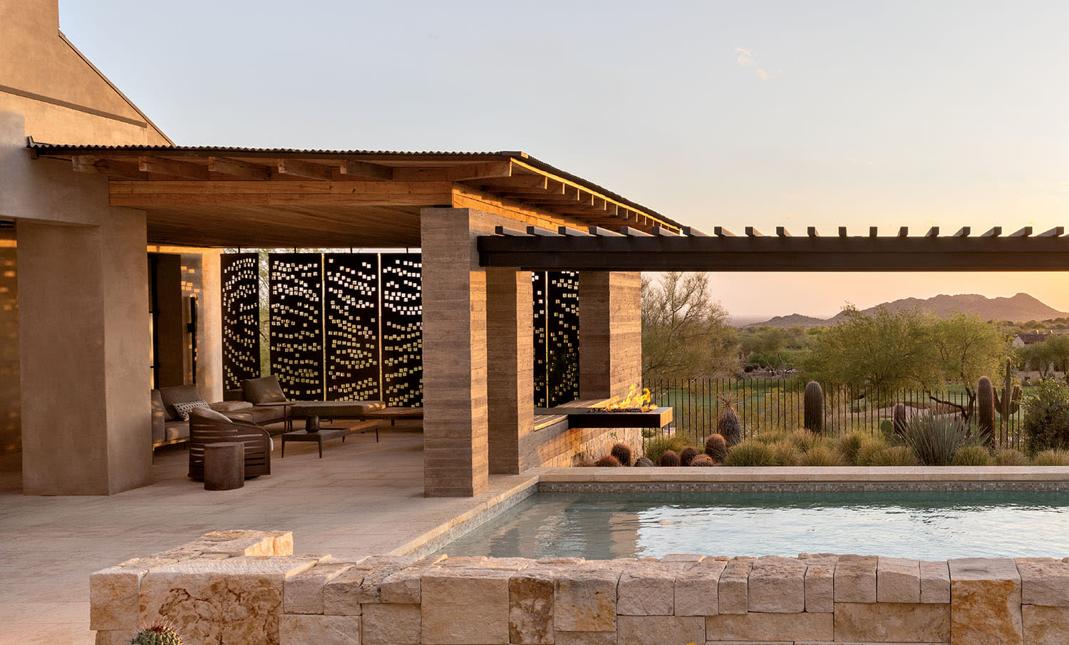 An outdoor swimming pool looks out at the mountains, near a patio with steel panels and seating.