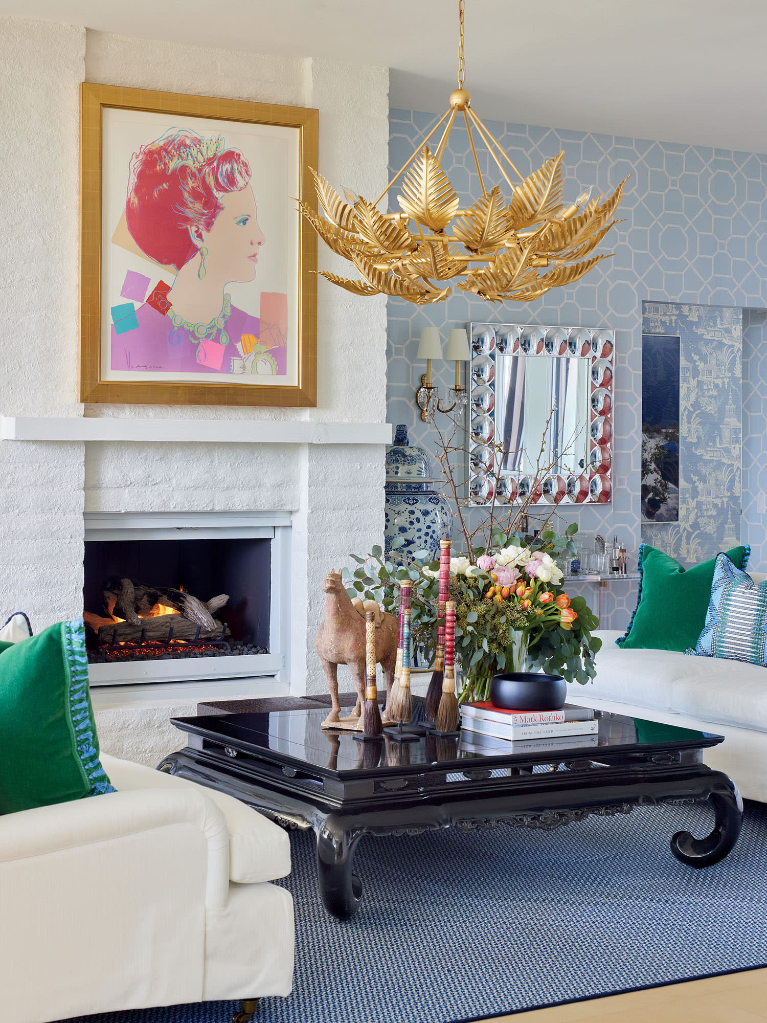 Stylish living room with a white fireplace, colorful portrait, and gold leaf chandelier. 