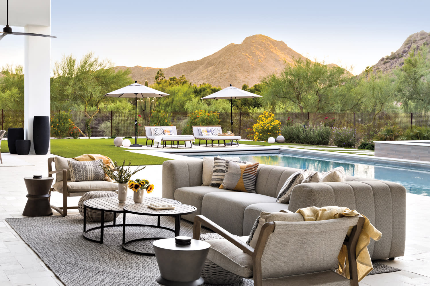 A patio seating area with a pool with loungers in the background and mountain views by Lindsay Kadlick