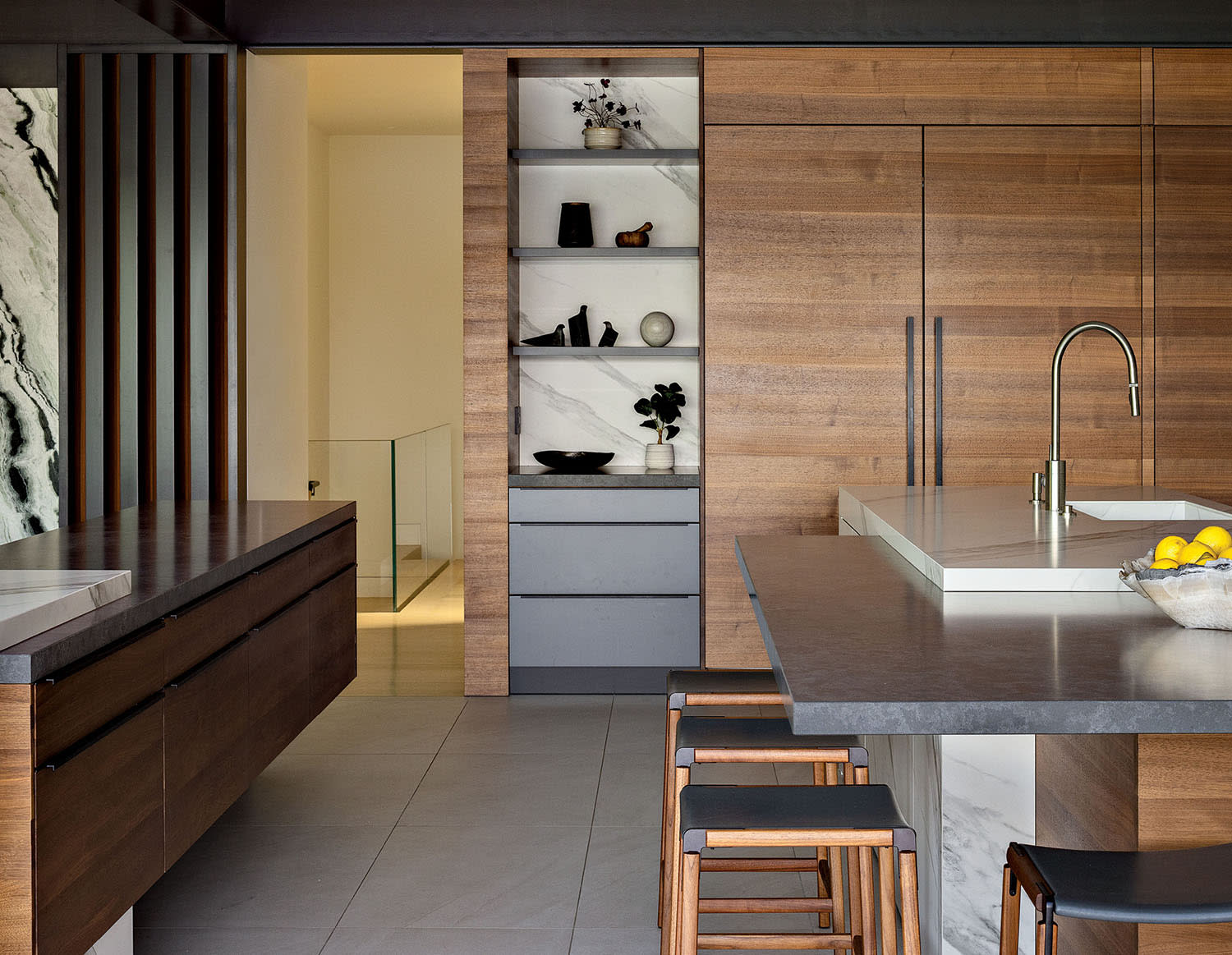 A kitchen outfitted in wood cabinets with black hardware and a center island with stools.