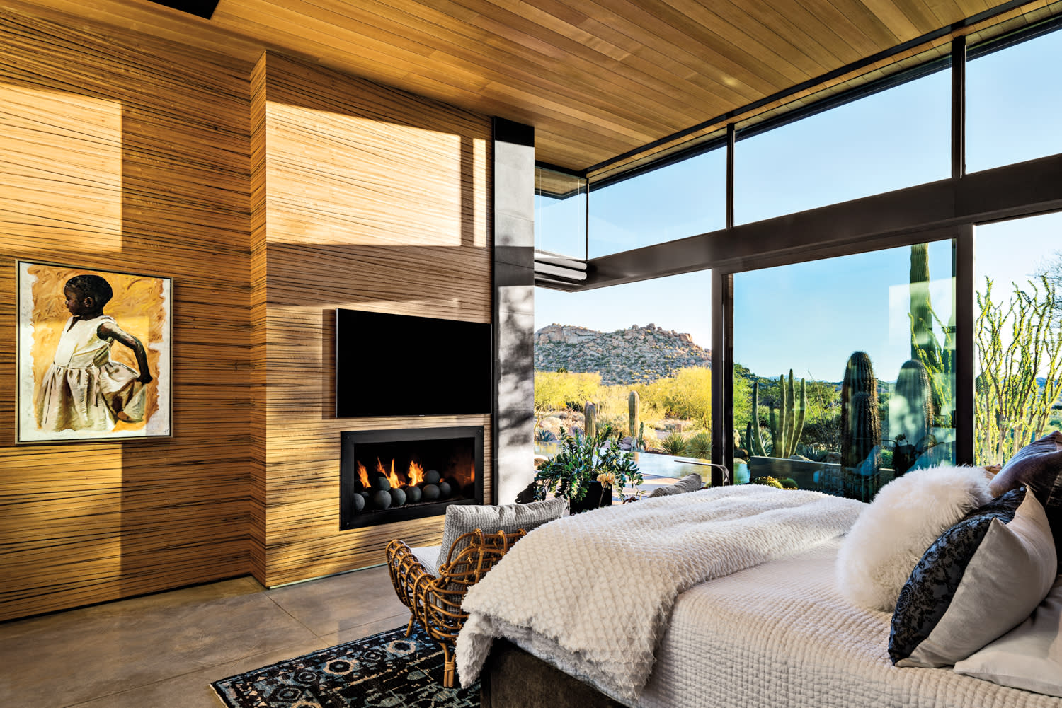 Wood-paneled bedroom with floor-to-ceiling windows and a modern fireplace by Sue White Heinz