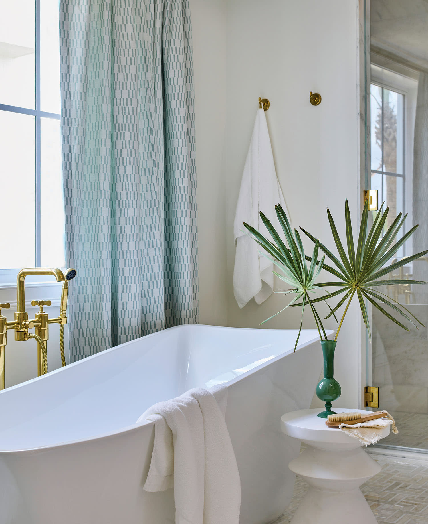 Modern bathroom with a white freestanding tub, gold fixtures, and a geometric curtain.