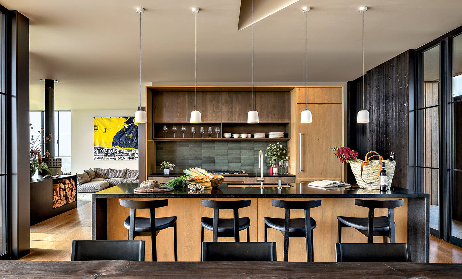 An open kitchen with an island set with four stools. Behind, a cooking area with tile backsplash.