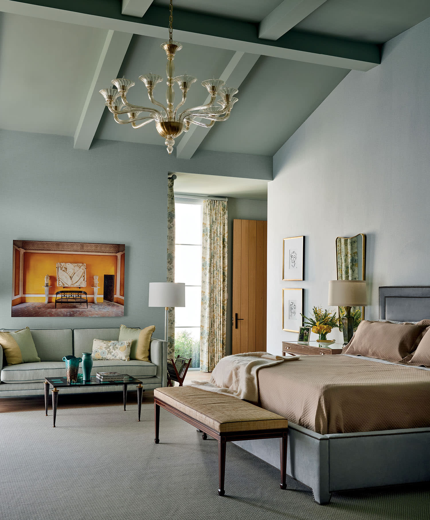 Elegant bedroom with blue-green walls and ceiling, featuring a chandelier, large bed, sofa, art, and lamp-lit side tables. A serene and cozy vibe.