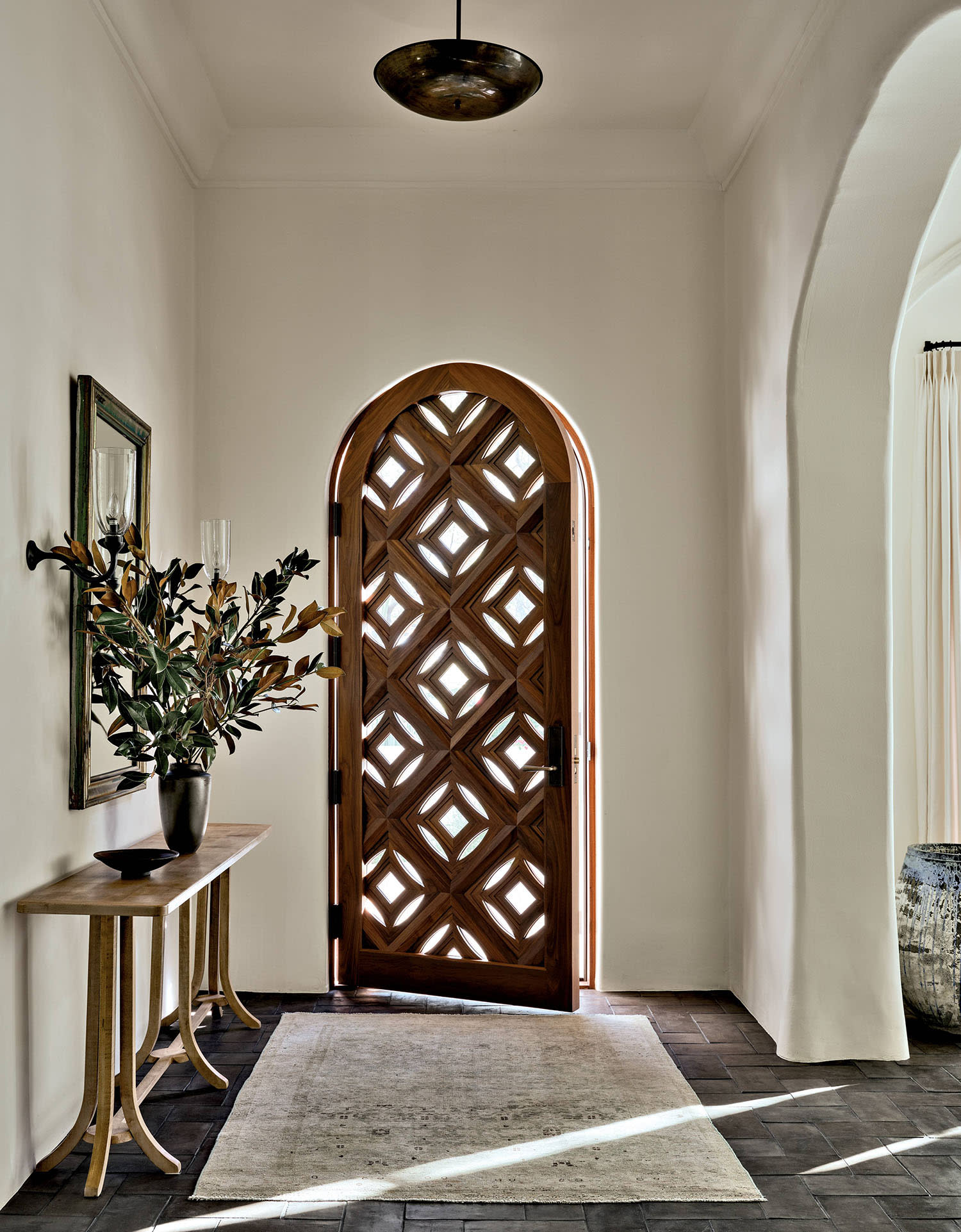 A front door with geometric cutouts opens into a white-walled entryway with console table and rug.