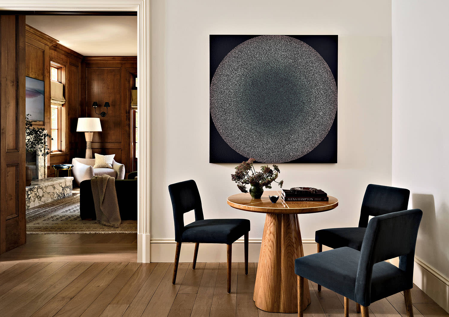A table with three chairs sits in a corner near a doorway with a glimpse of a marble fireplace.