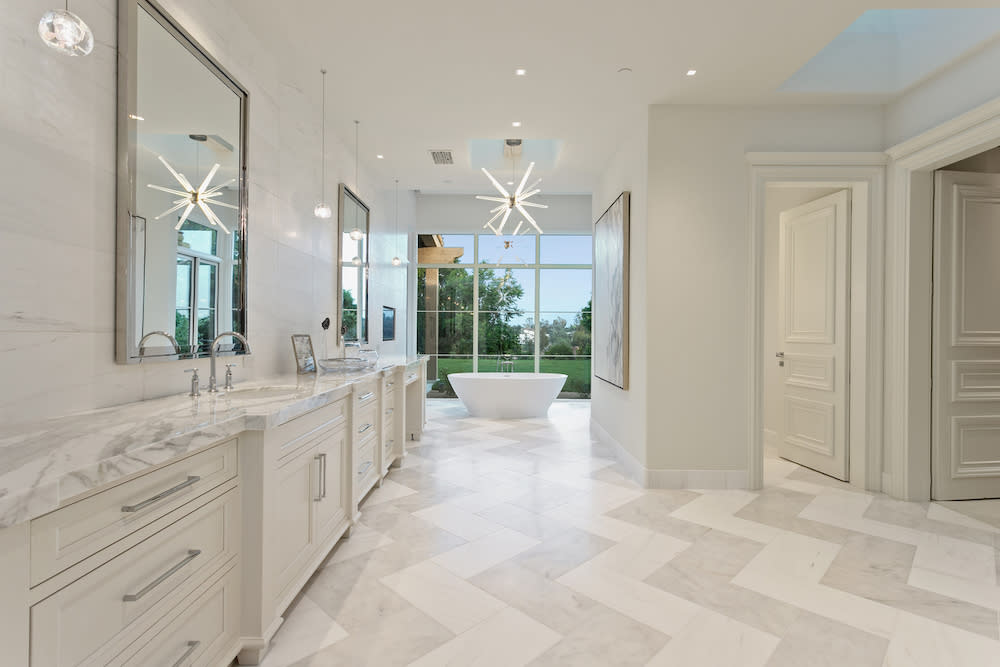 Luxurious bathroom with white chevron marble floors, white cabinets and large tub.