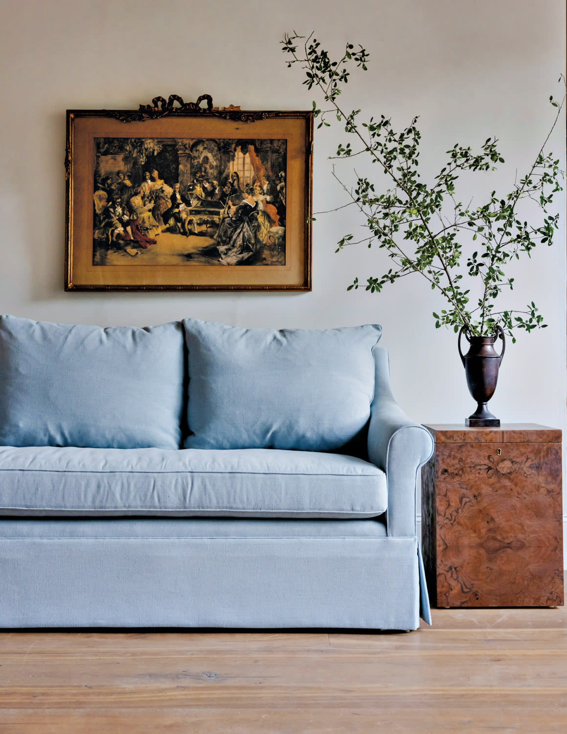 Blue sofa underneath an antique artwork and next to a brown marbled side table.