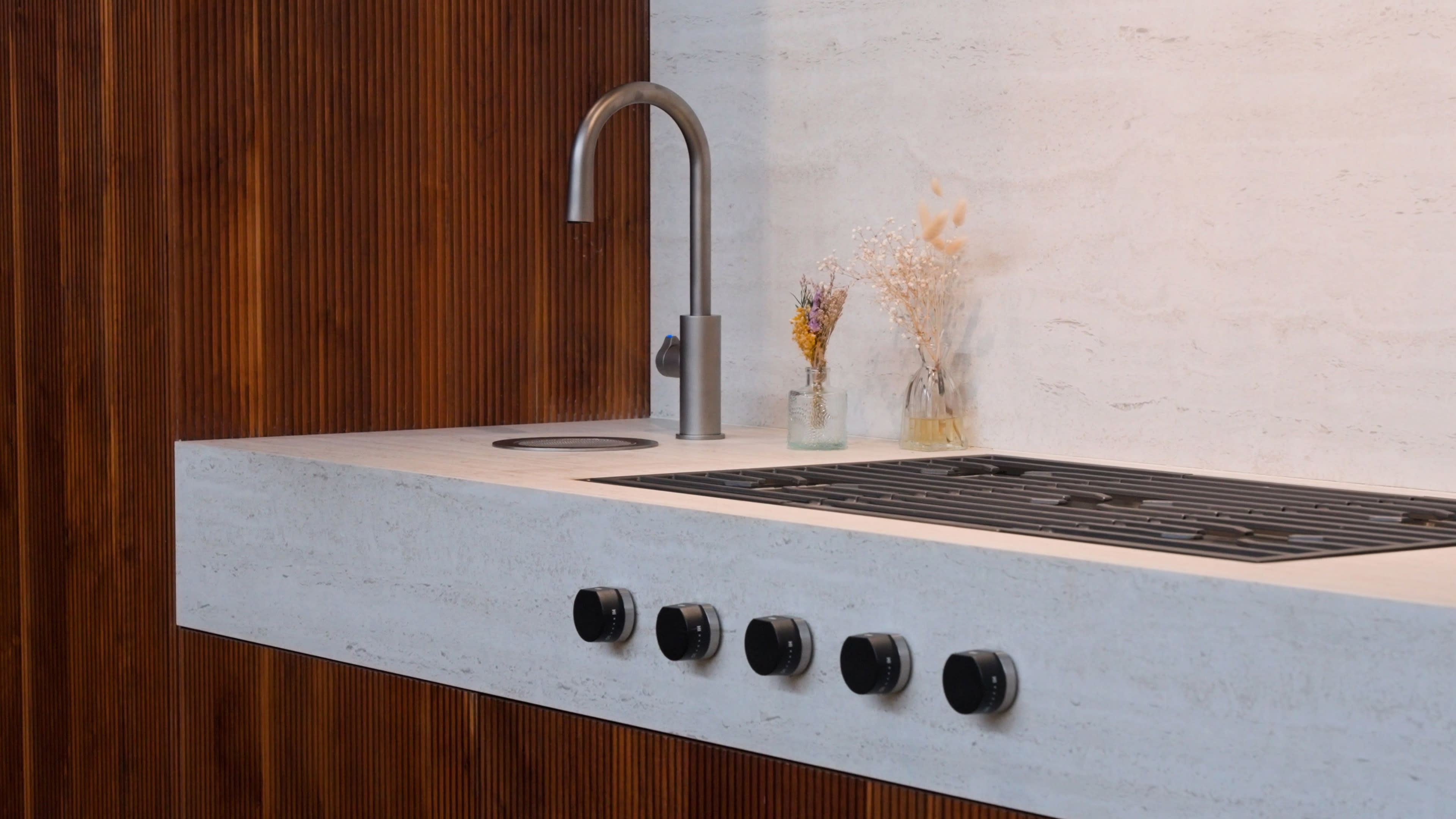 Modern kitchen with sleek faucet, white countertop, and gas stove. Wooden paneling adds warmth. Dried flowers in vases provide a touch of elegance.
