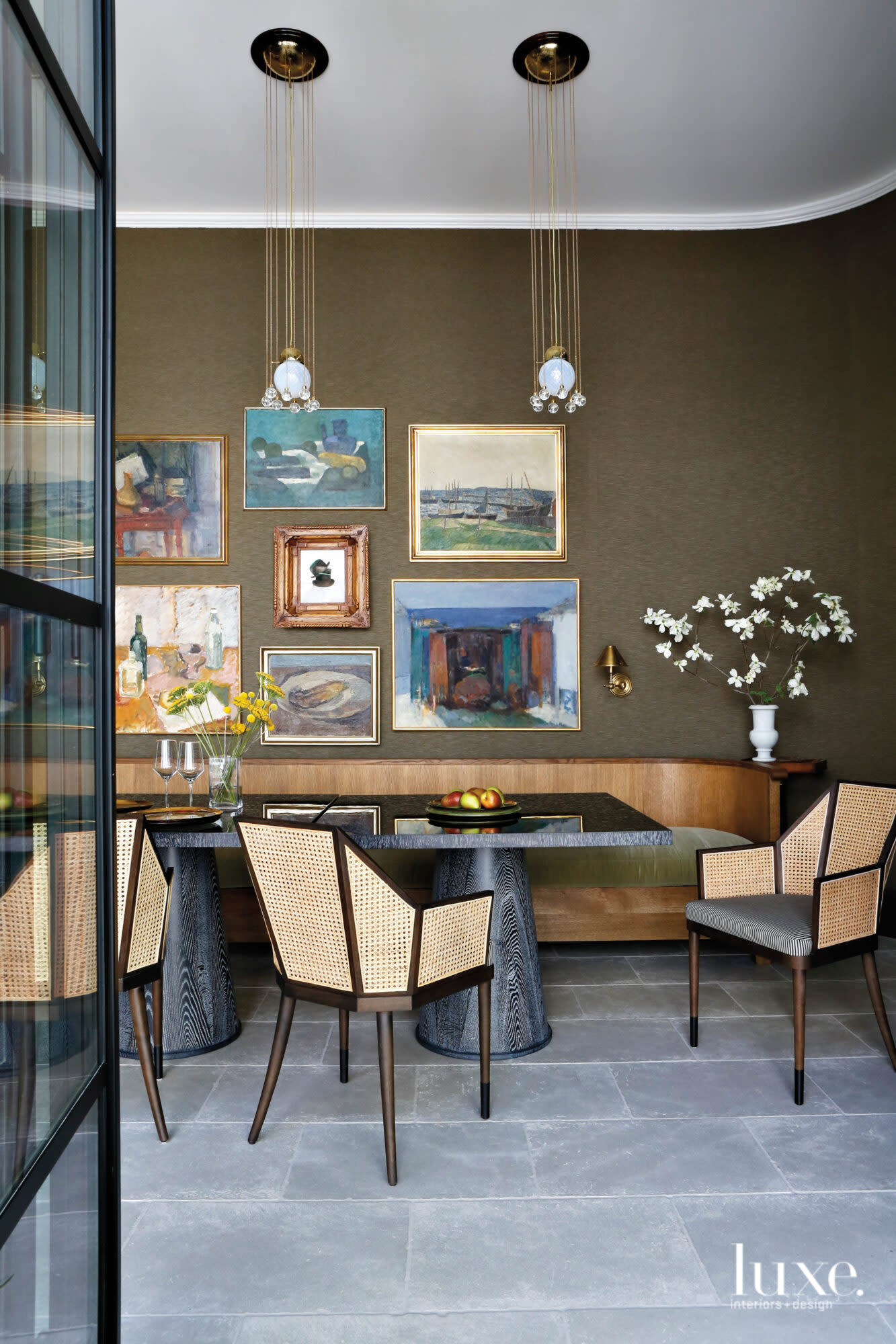 A dining room with a curved banquette, dark silk wall covering, modern armchairs and mismatched collage of framed wall art
