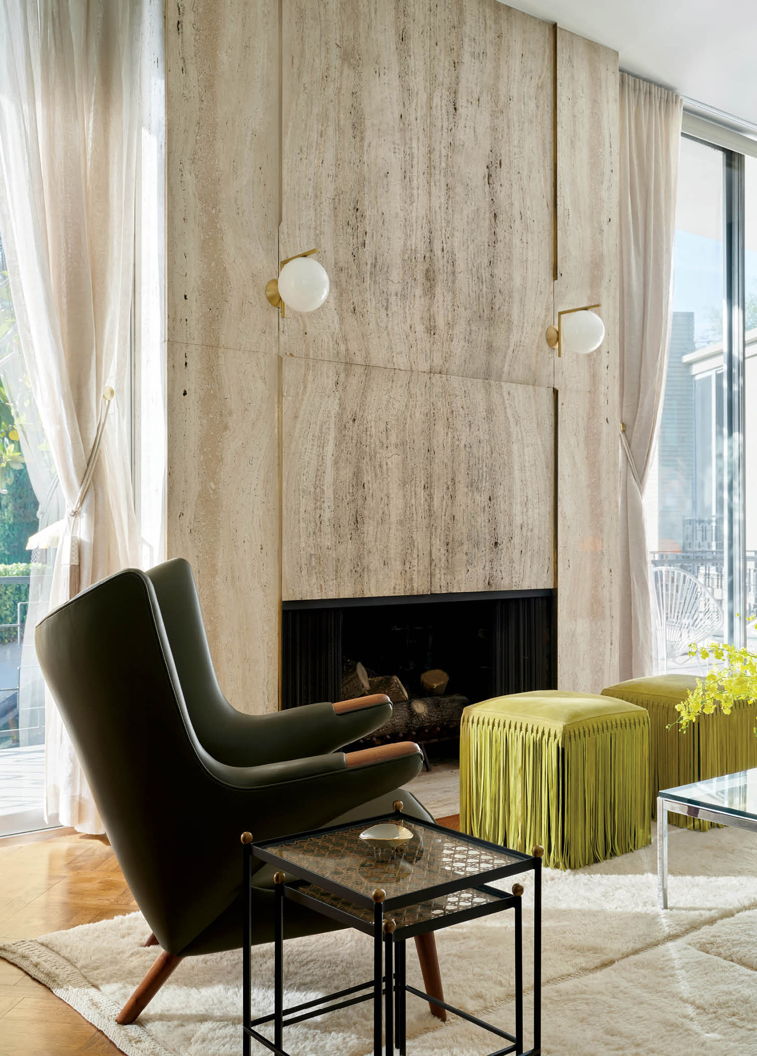travertine fireplace in a living room with a green leather chair and green fringed ottomans