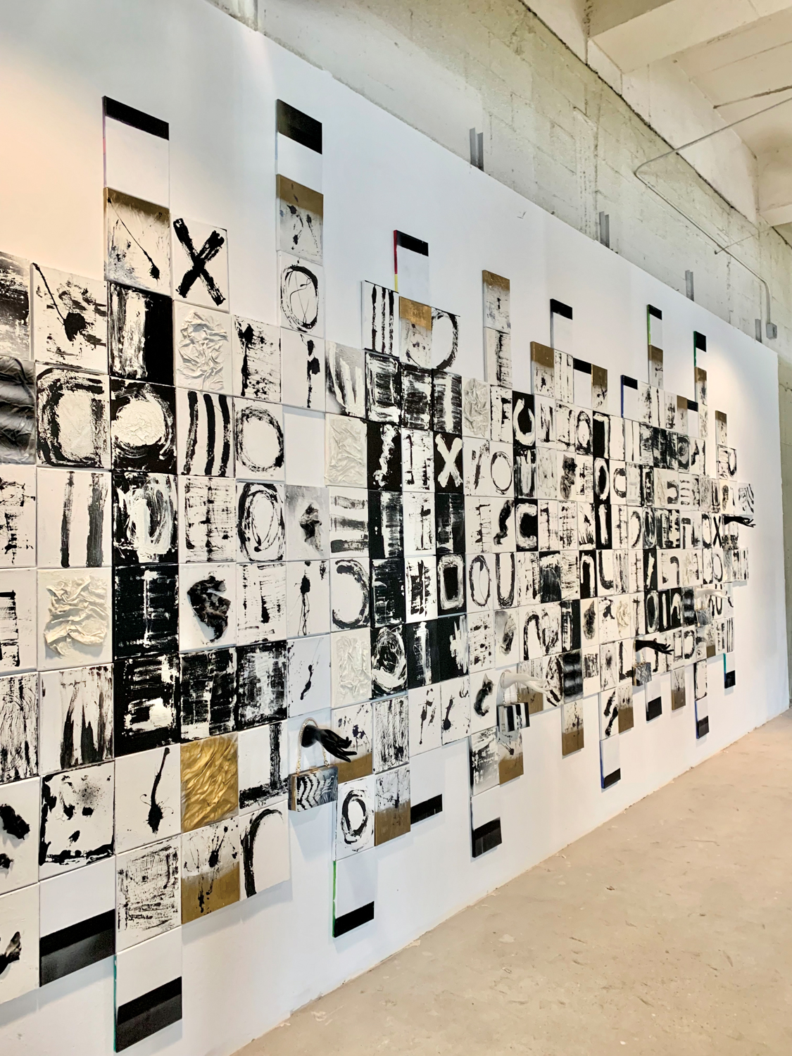 Assortment of black, white and gold mixed media artworks along a white wall