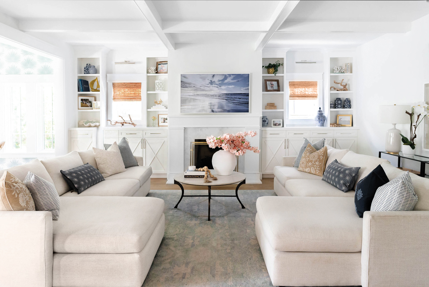 living room with two cream-colored sectionals, white walls and built-in, round coffee table and blue-toned rug