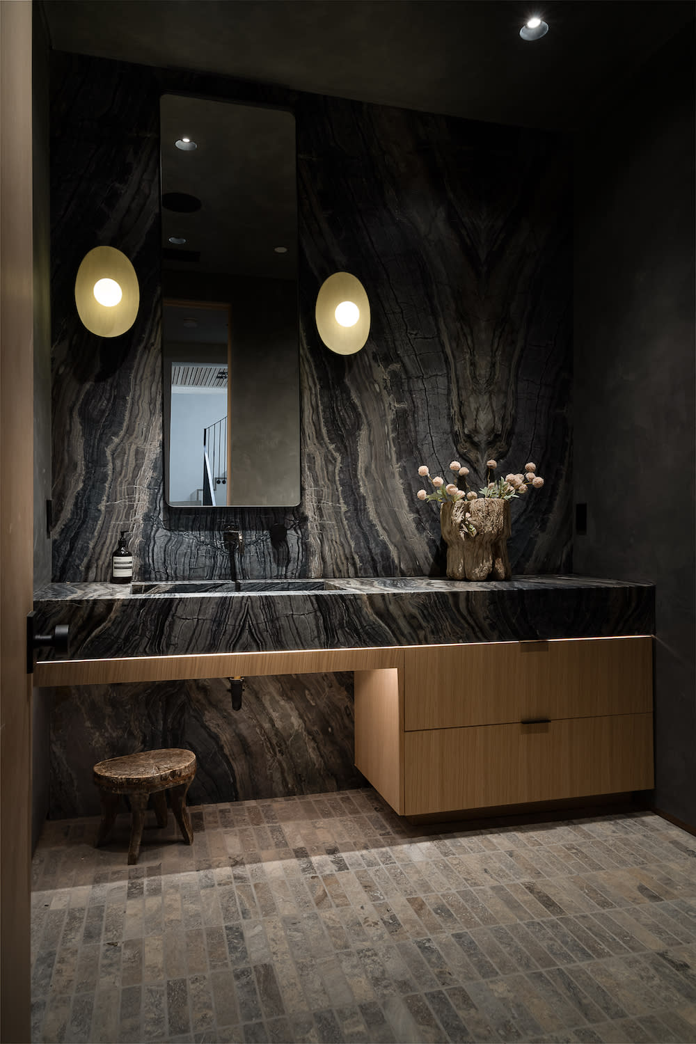 A luxurious bathroom featuring a sleek black marble wall and an elegant wooden counter, creating a sophisticated ambiance.