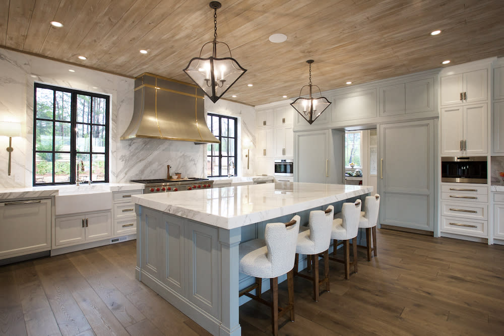 large kitchen with marble countertops, white barstools and white cabinets with black windows by Construction Resources in Georgia