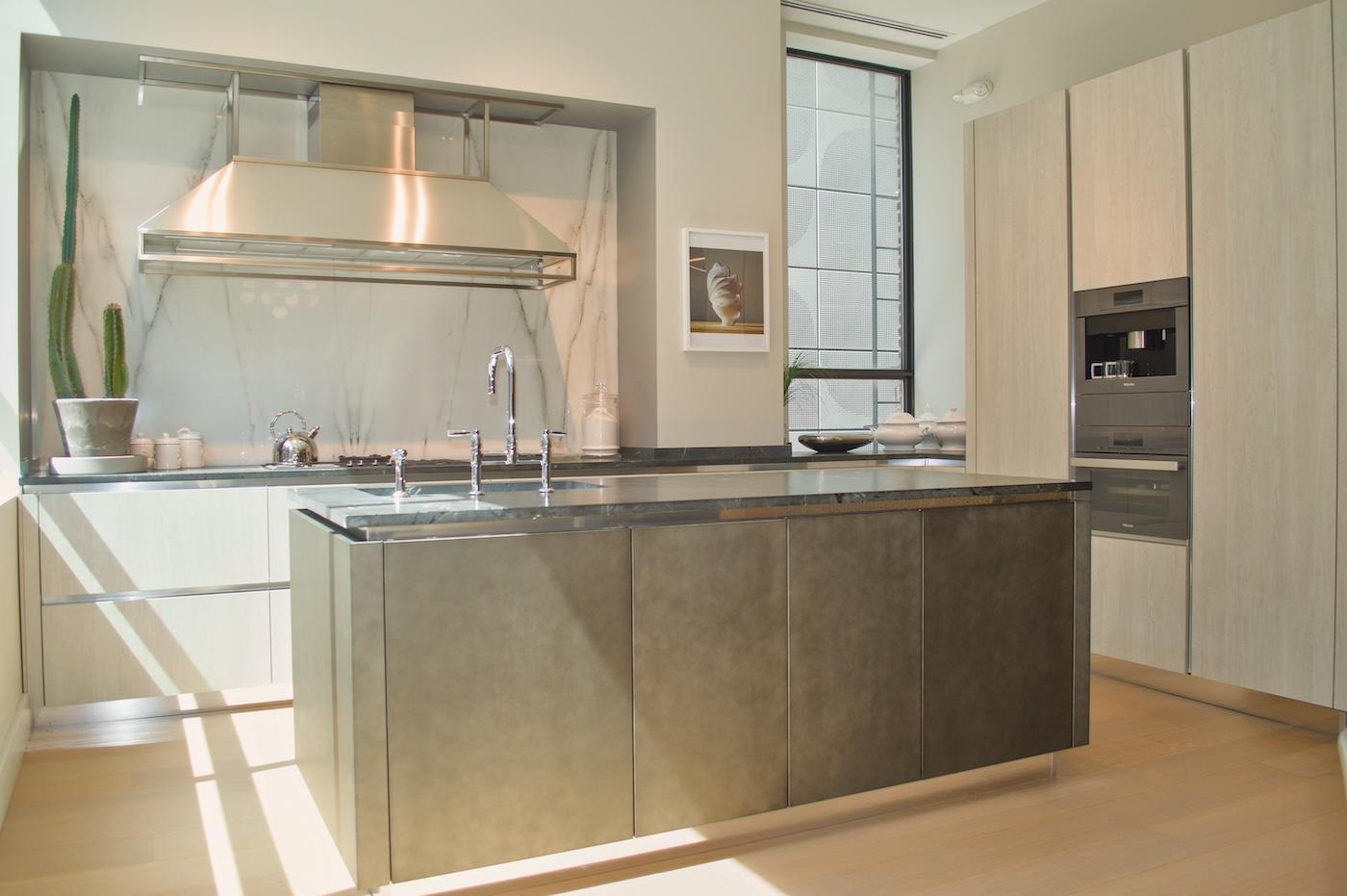 Modern kitchen with a central island and sleek metallic surfaces. A large window allows sunlight to illuminate the space, giving it a warm ambiance.