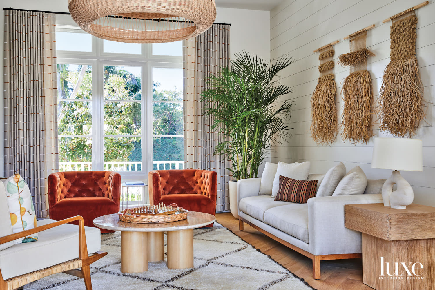 living area with burn-orange armchairs, white sofa, raffia chandelier and wallcoverings