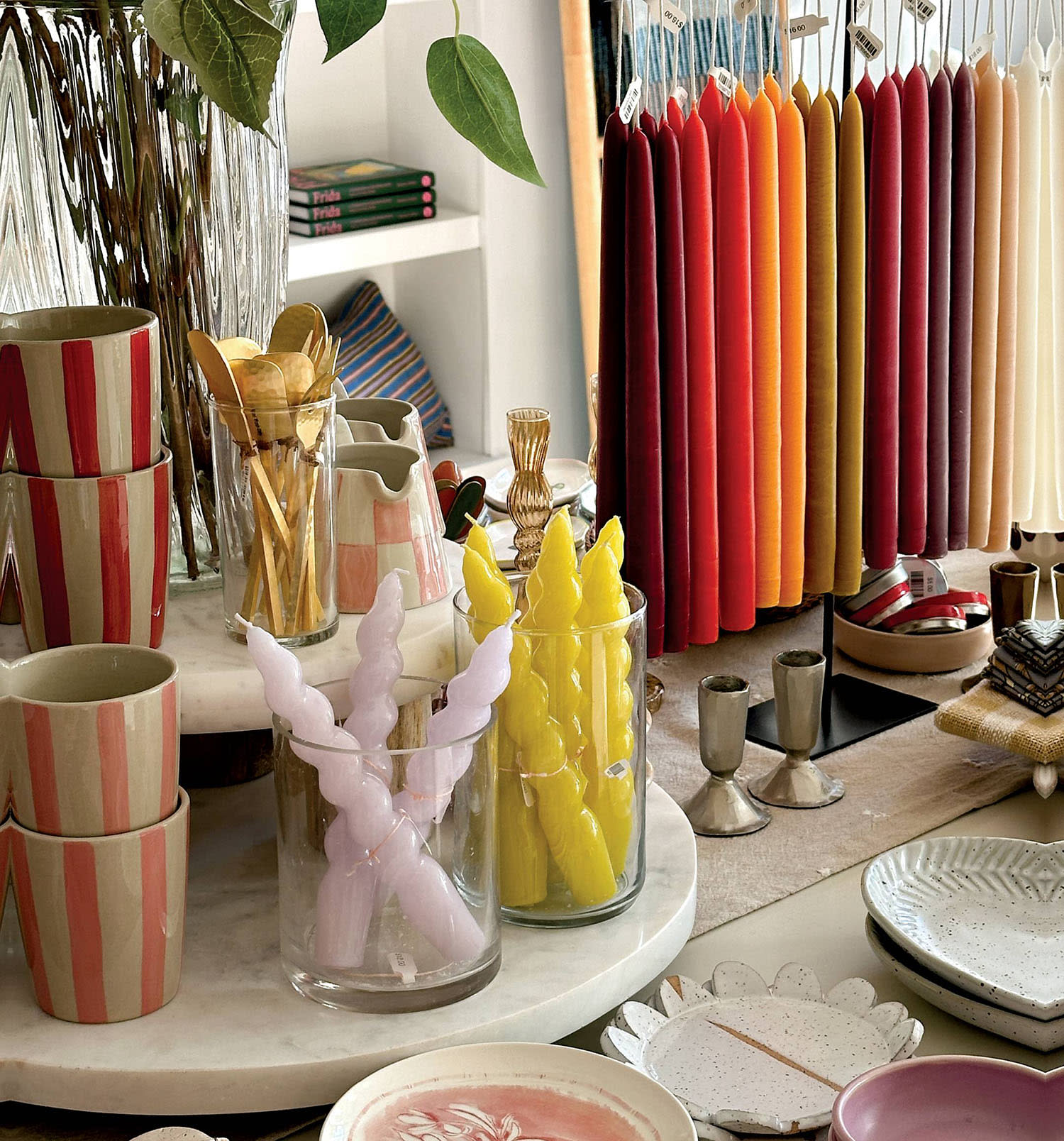 Colorful candles displayed in jars and hanging by their wicks on a store table.