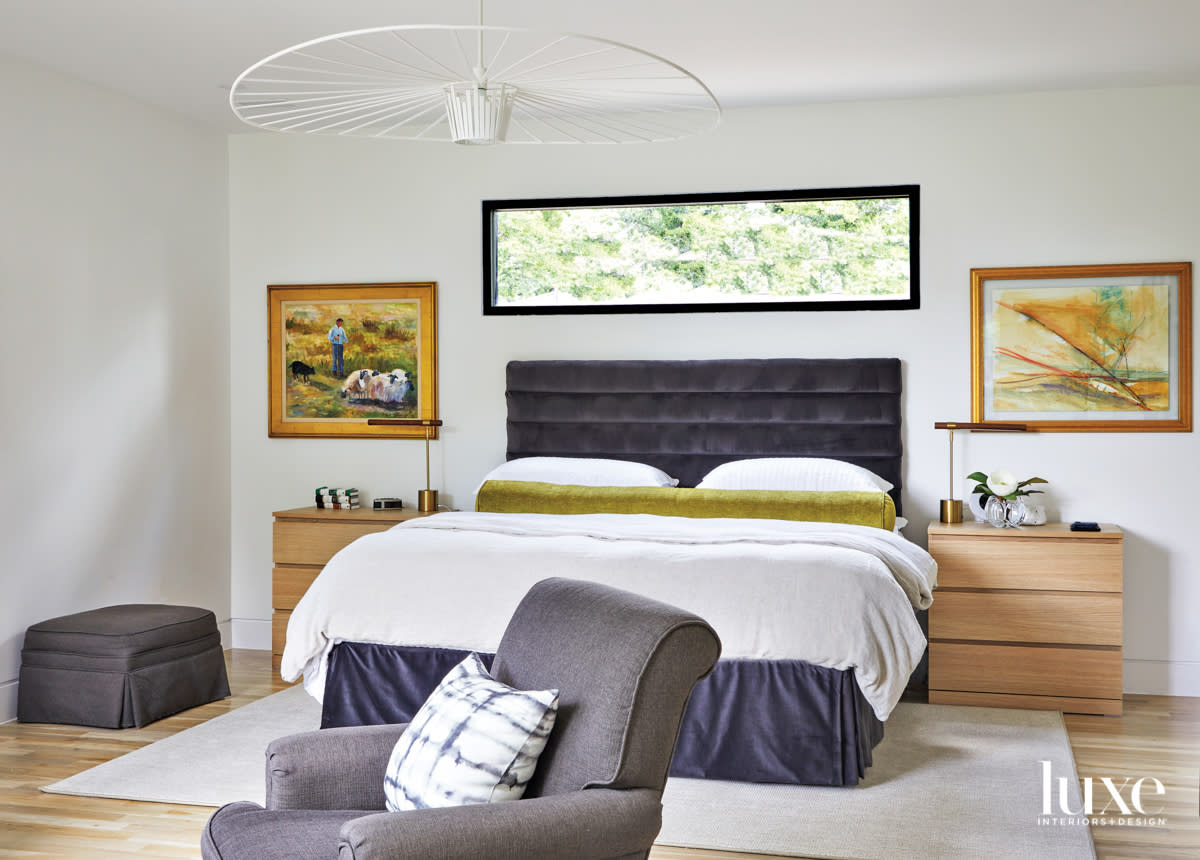 Minimalist bedroom with charcoal upholstered bed, modern ceiling fixture and traditional artwork