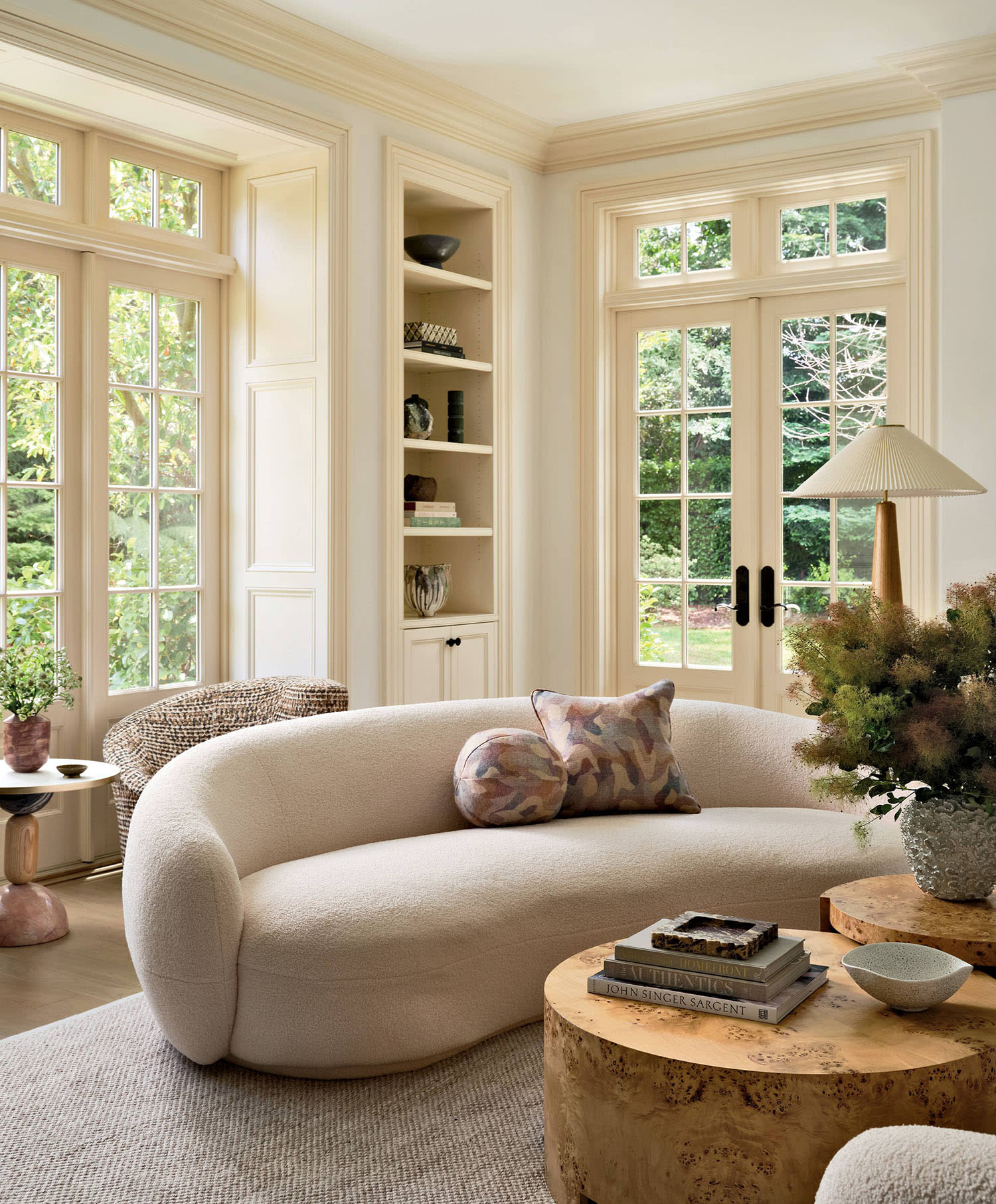 A bouclé sofa topped with pillows sits near two coffee tables, a floor lamp and built-in shelves.