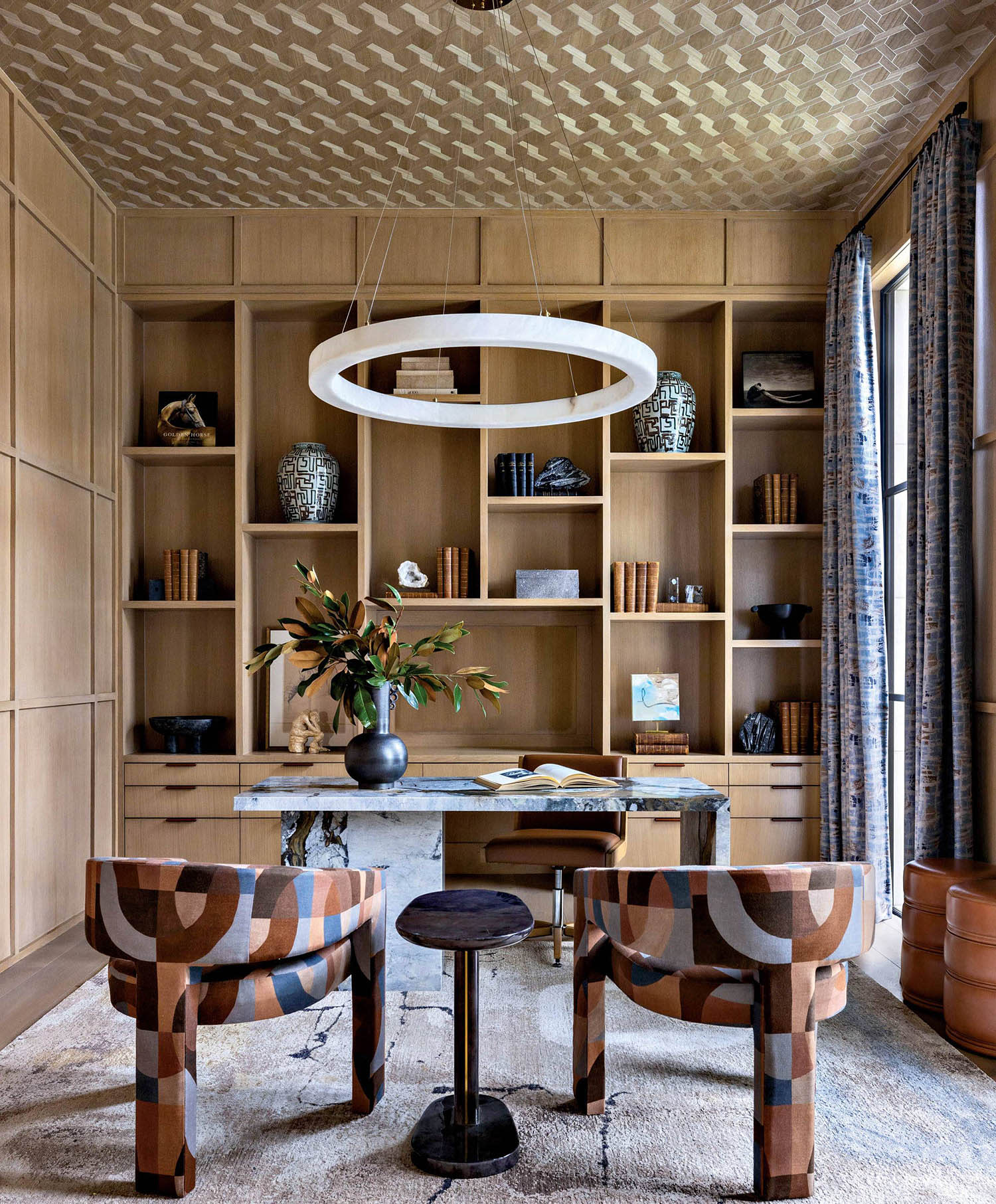 A stone desk sits in an office flanked by two chairs with a patterned wallcovering on the ceiling.