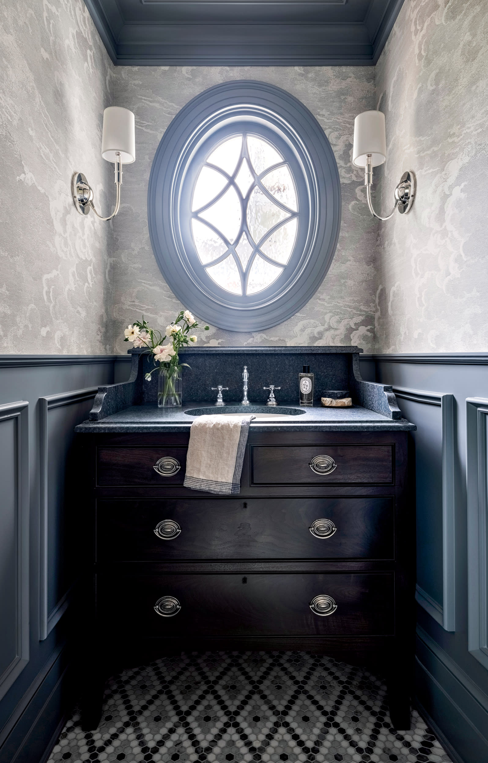 an oval shaped window above a dark sink in a vintage-inspired powder room