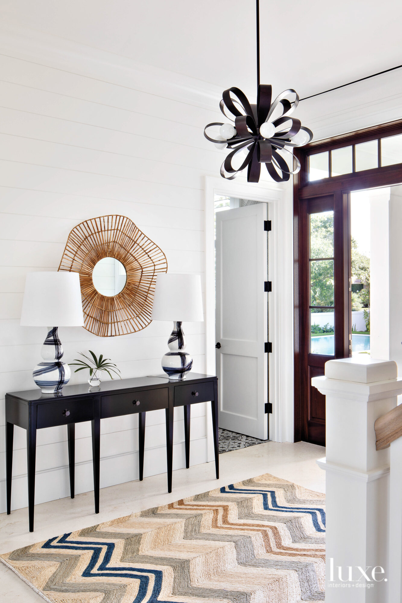 A foyer with a metal chandelier over a multi-color striped rug.