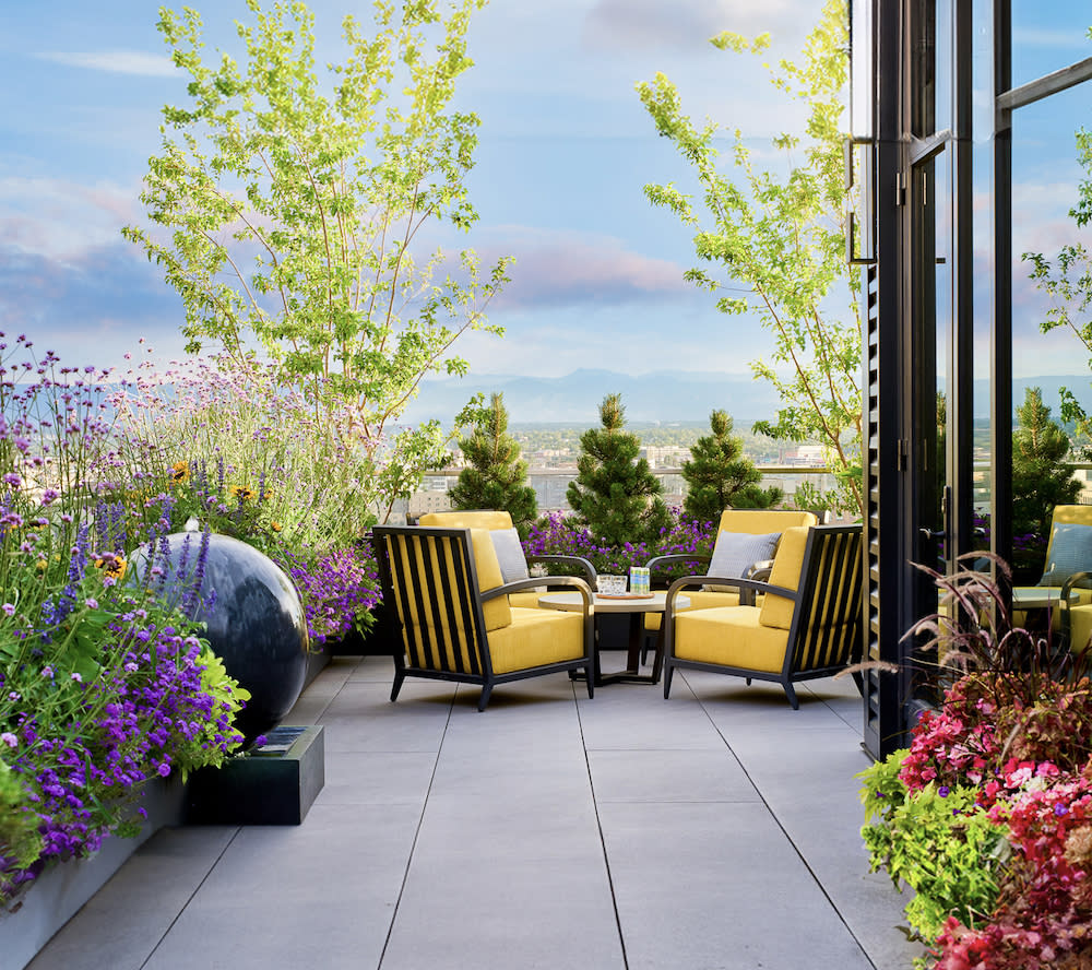 Outdoor patio with colorful flower and plant border. Seating area with cheerful yellow chairs.