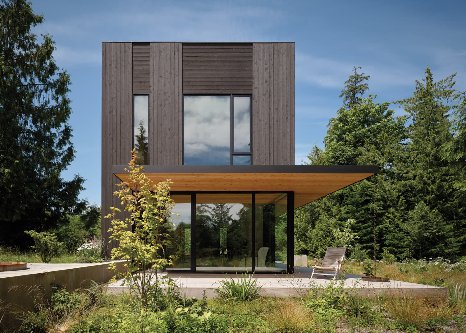 A sleek modern house with a spacious wooden deck and a vibrant landscape