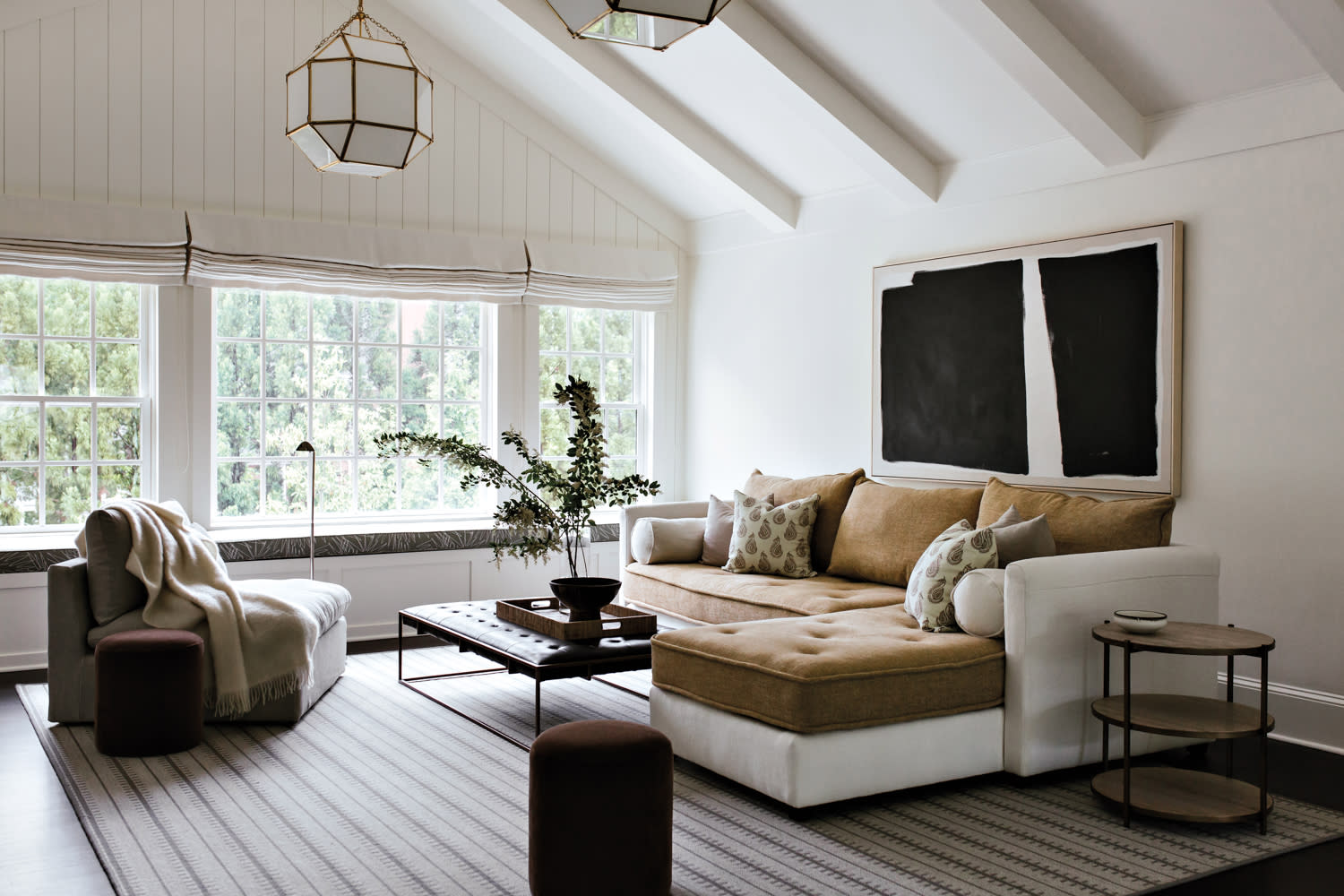 Lounge space with sectional, black abstract artwork, striped rug and opaque glass hanging lanterns