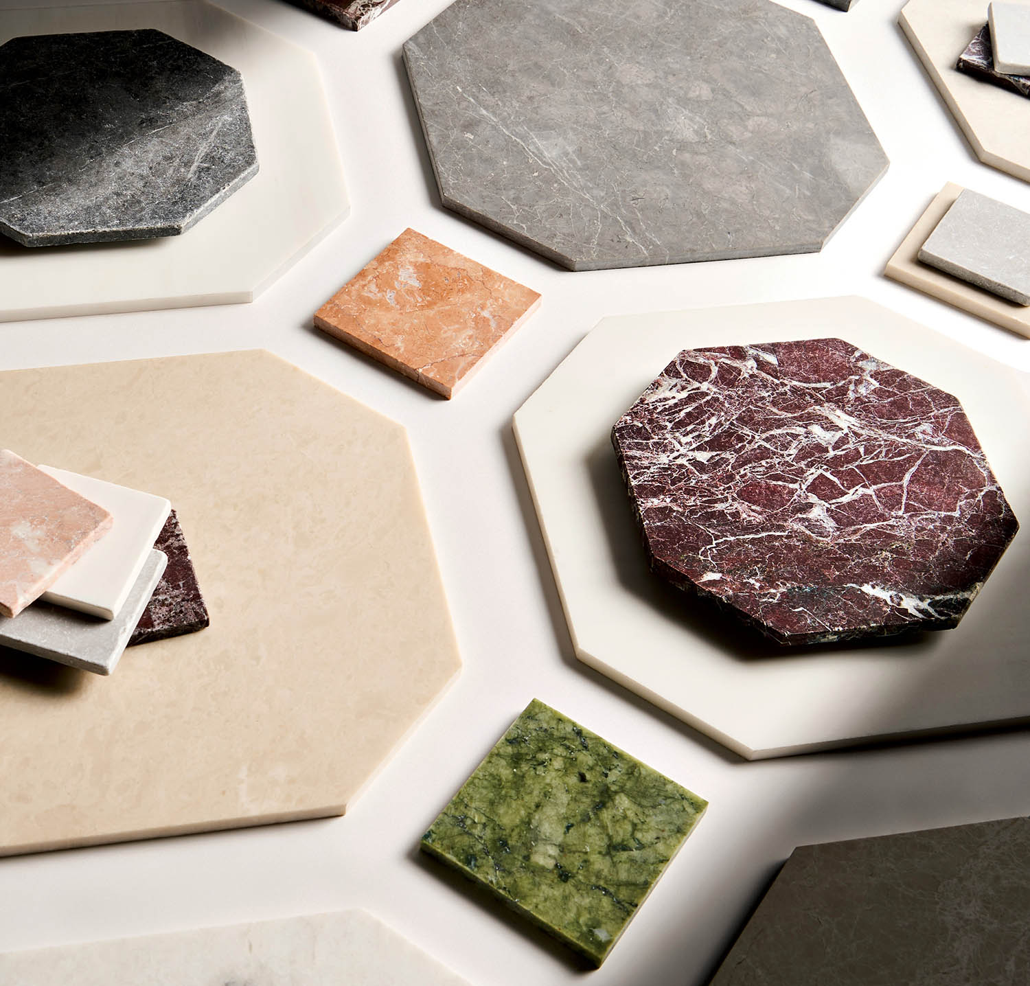 Assorted hexagonal and square marble tiles in various colors, including gray, beige, red, and green, arranged on a white surface, conveying elegance.