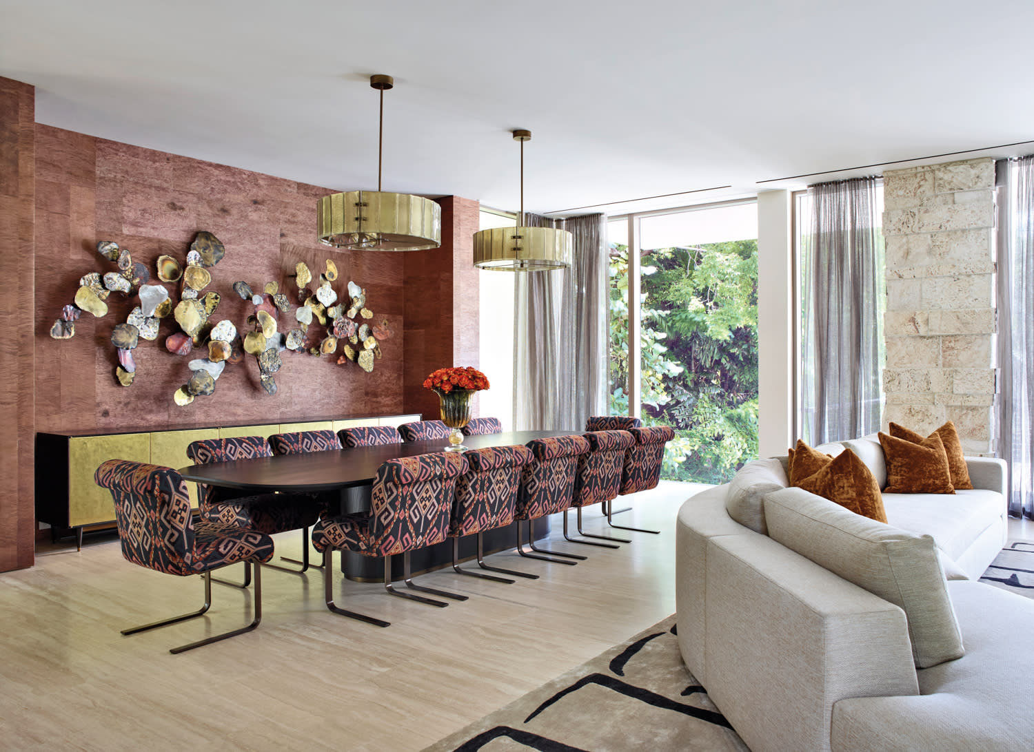 Elegant dining room with patterned chairs, a long table, and modern wall art. Soft lighting, cozy sofa, large windows, lush green view.