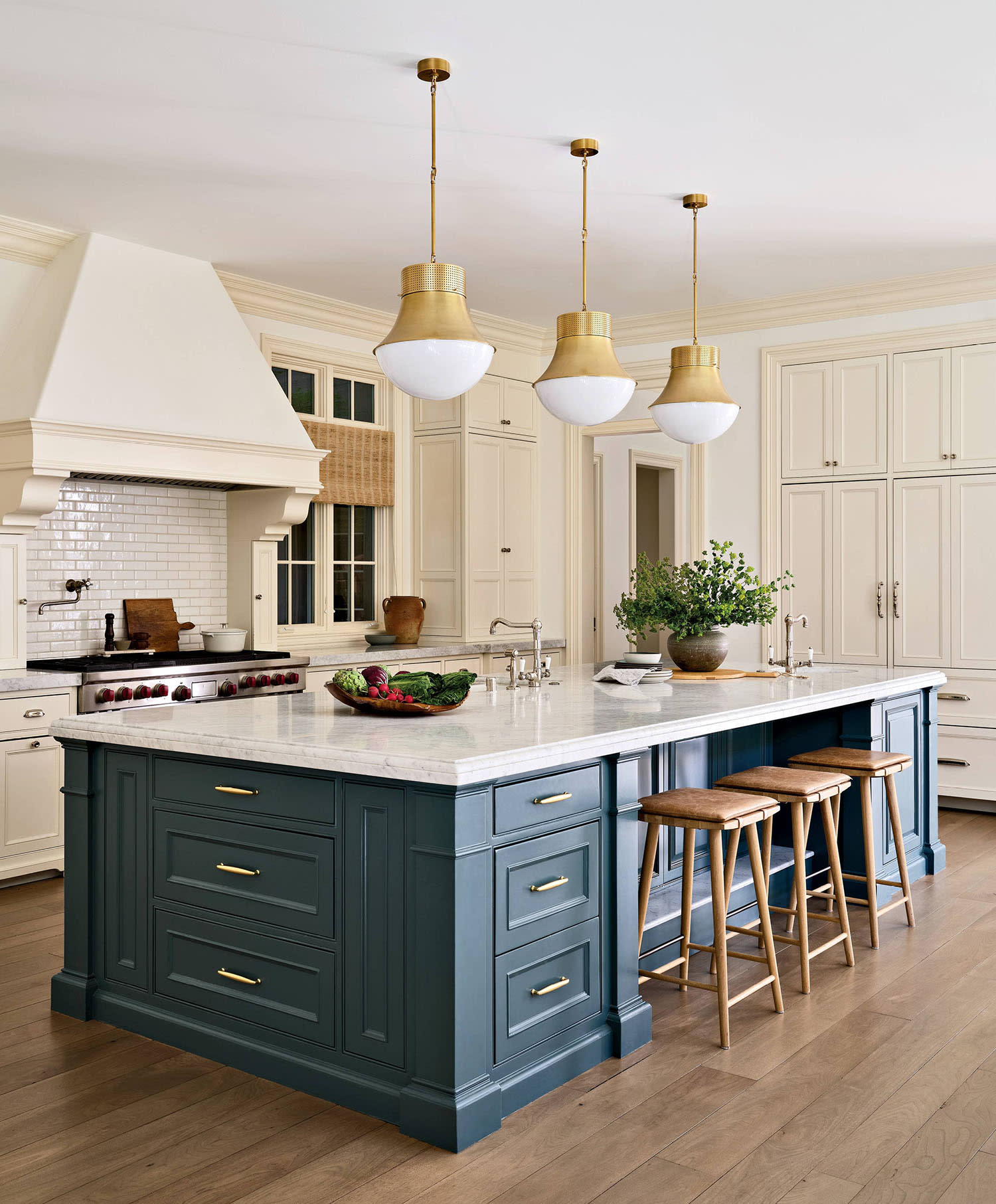 A trio of pendant lights hang over a kitchen island with blue cabinets and stools lining the counter.