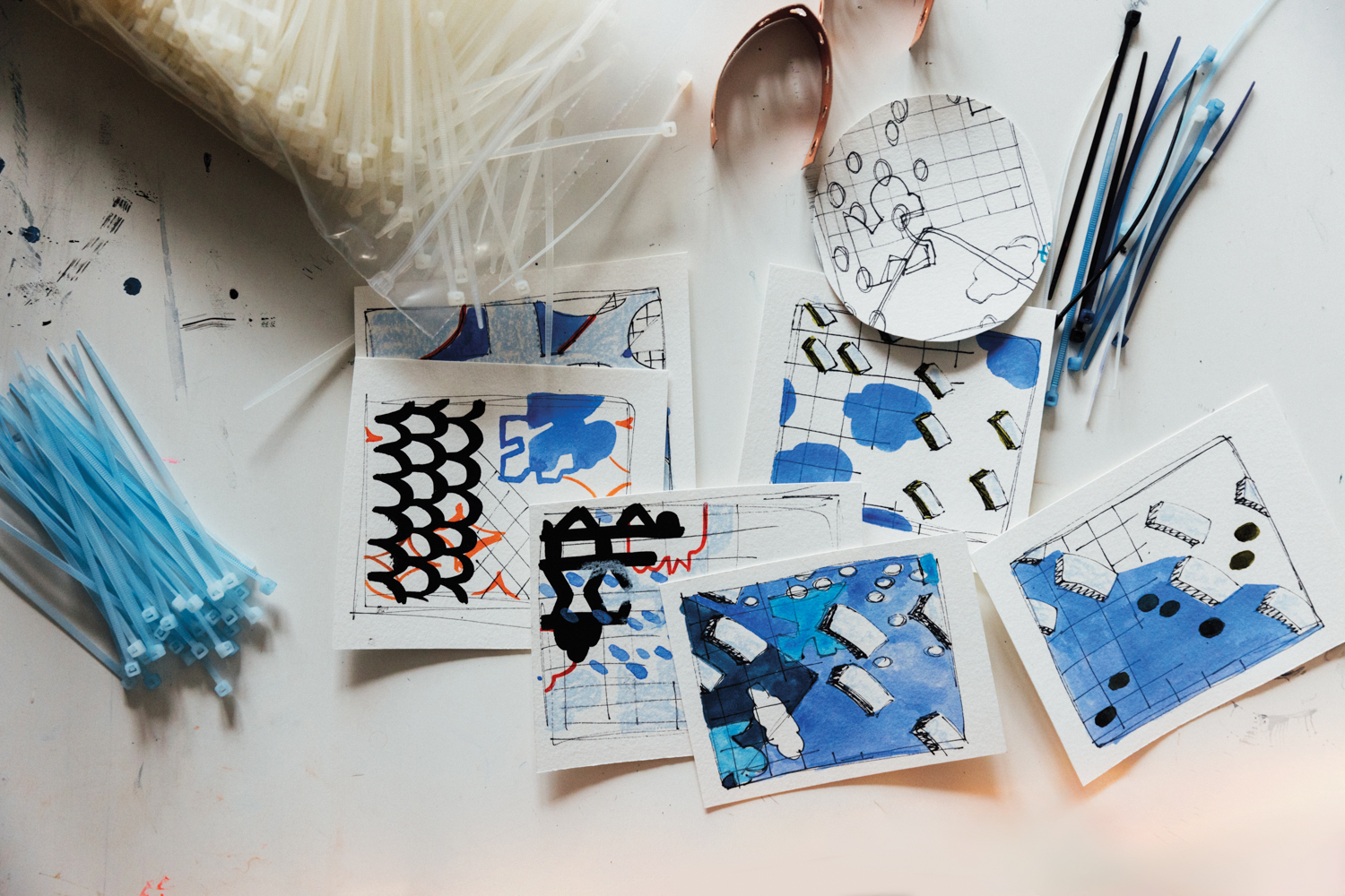 watercolor paintings, drawings and zip ties lay on a white table