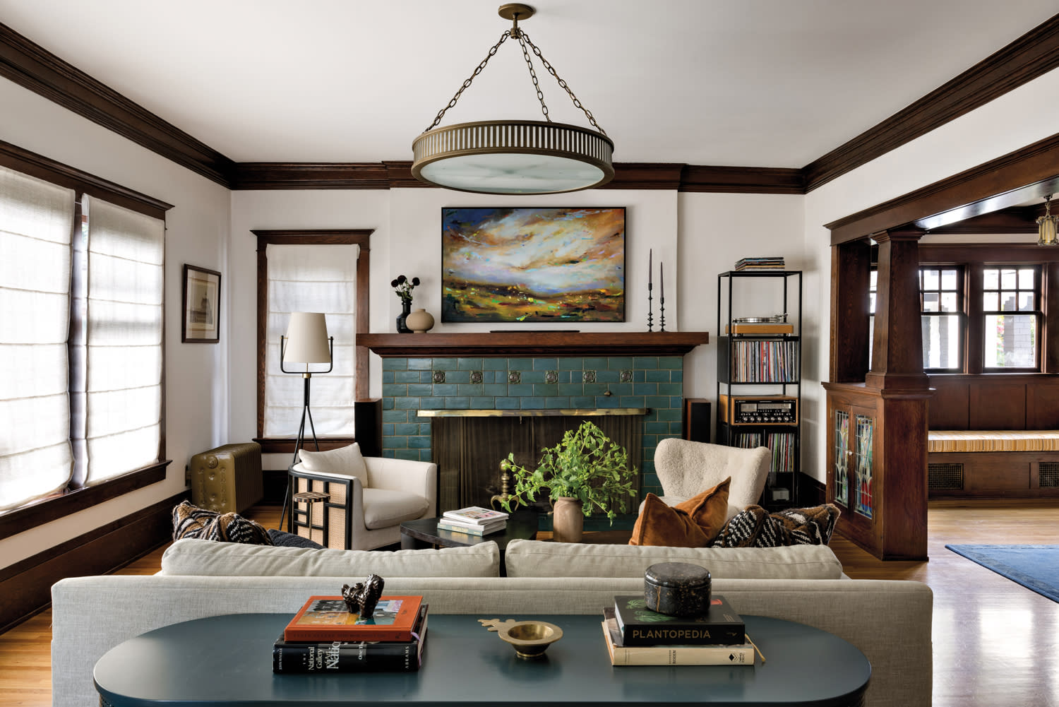 Living room with matching cane chairs, round light fixture, landscape painting and centered by a large tiled fireplace