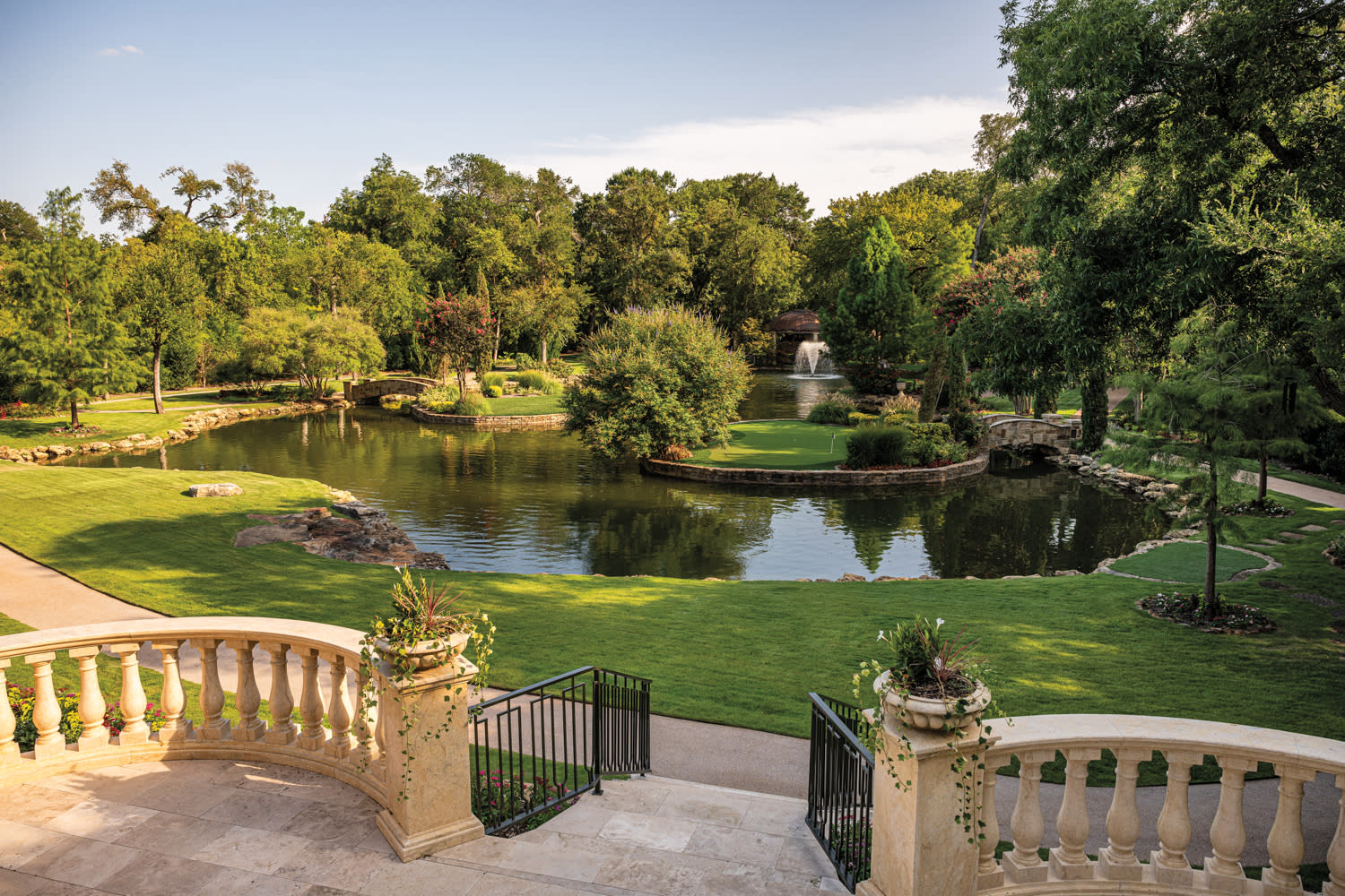 A serene garden with a large pond, surrounded by lush trees and manicured lawns. Stone steps and balustrades lead to this peaceful, picturesque scene.