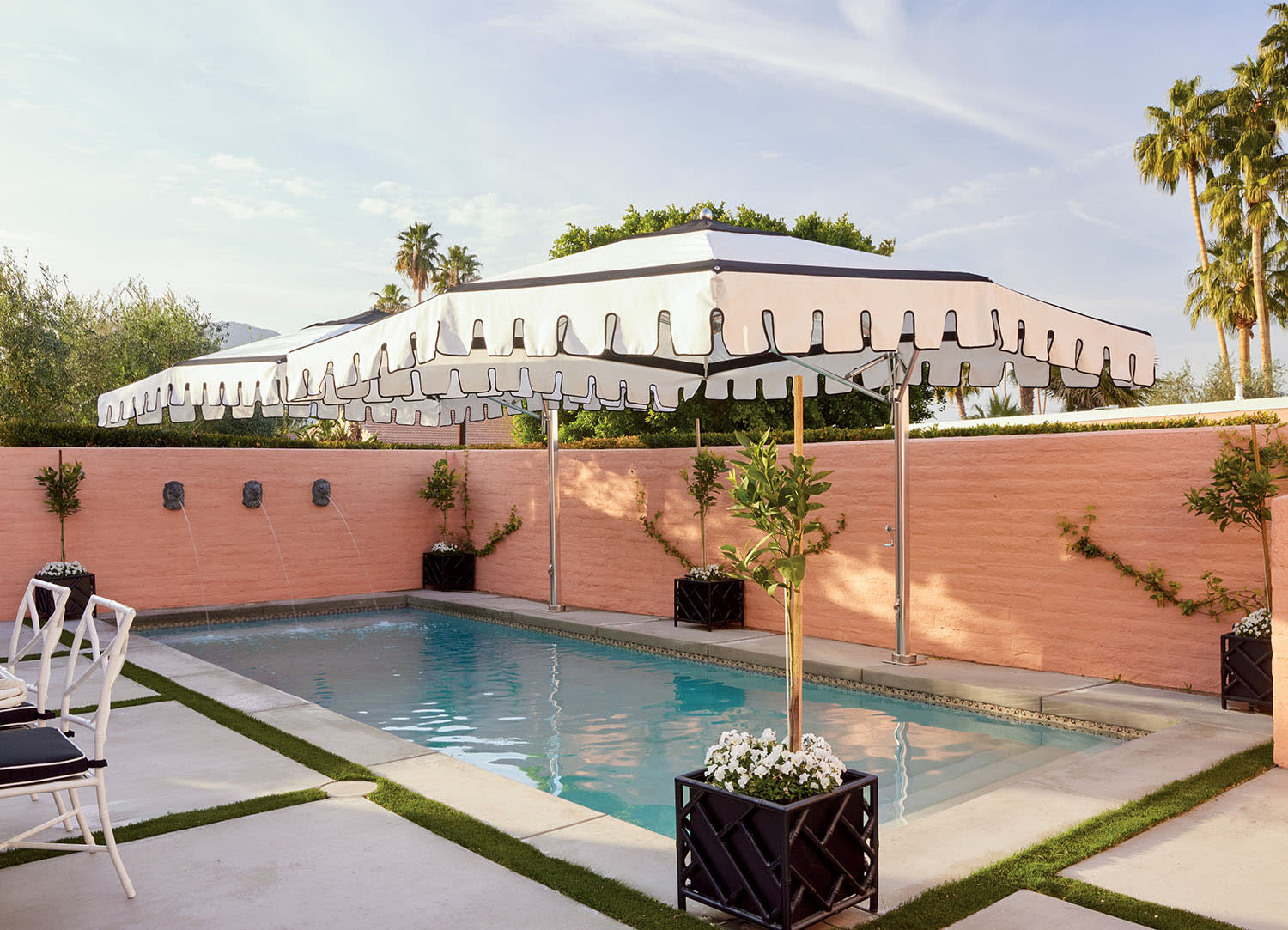 Elegant pool area with striped umbrellas and pink walls adorned with small fountains