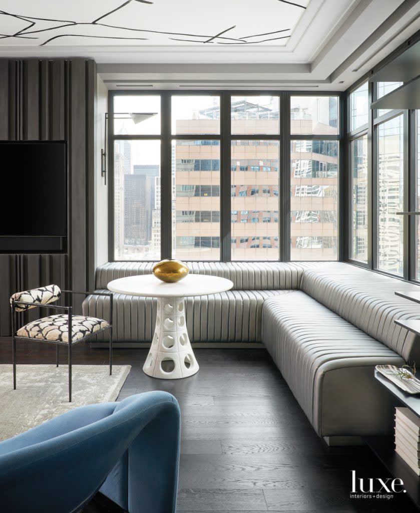 The condo's deep window seats, in channel-stitched Romo fabric, also serve as seating for a casual dining area completed by an Arteriors chair and a Global Views table. The sconce is by Circa Lighting. Artistic Construction fabricated the adjacent media wall.