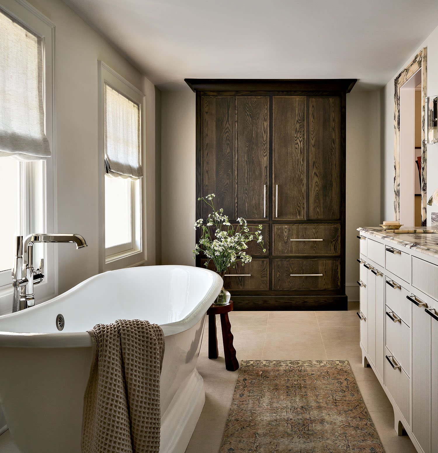 Elegant bathroom with a freestanding white tub, wooden cabinet, and marble countertop.