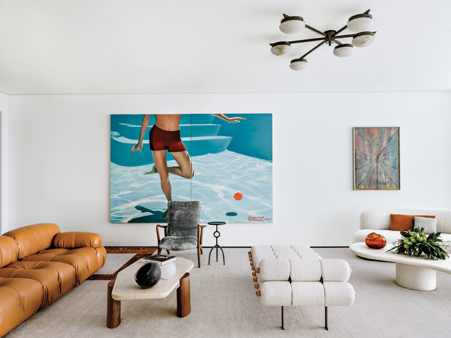 Living area with swimming pool artwork, white bench, tan sofa and globe chandelier