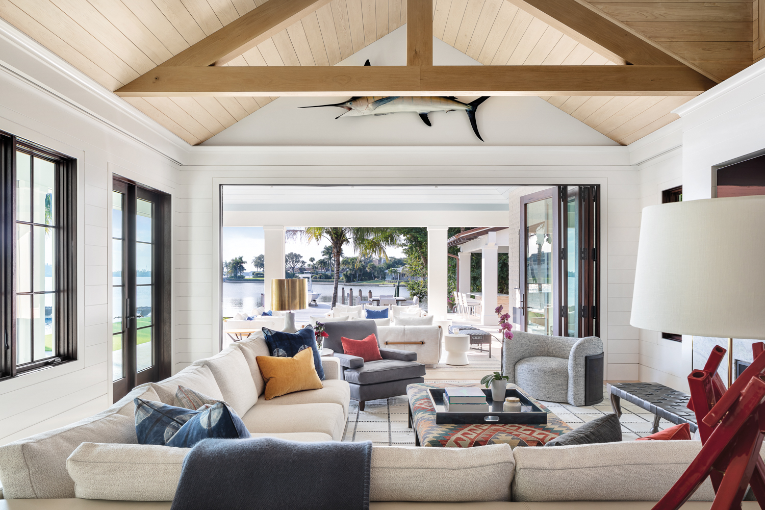 living area with cream-colored sectional, red lamp and pitched wood ceiling